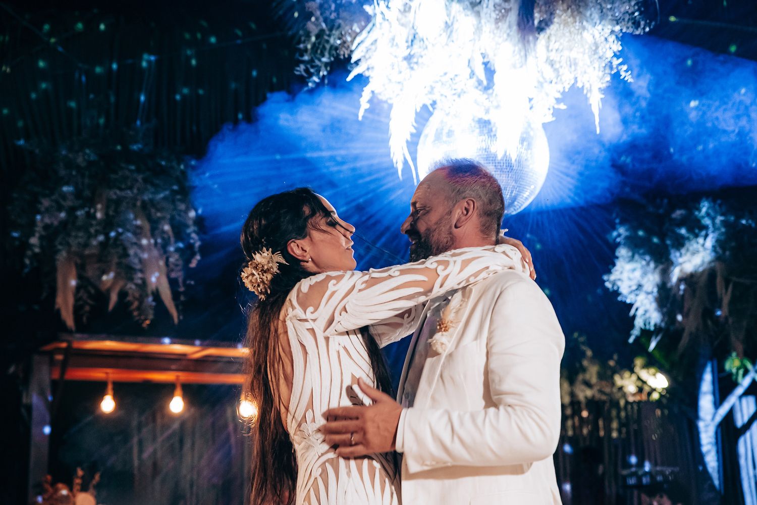 A couple embraces during their first dance beneath ethereal blue lighting and sparklers.
