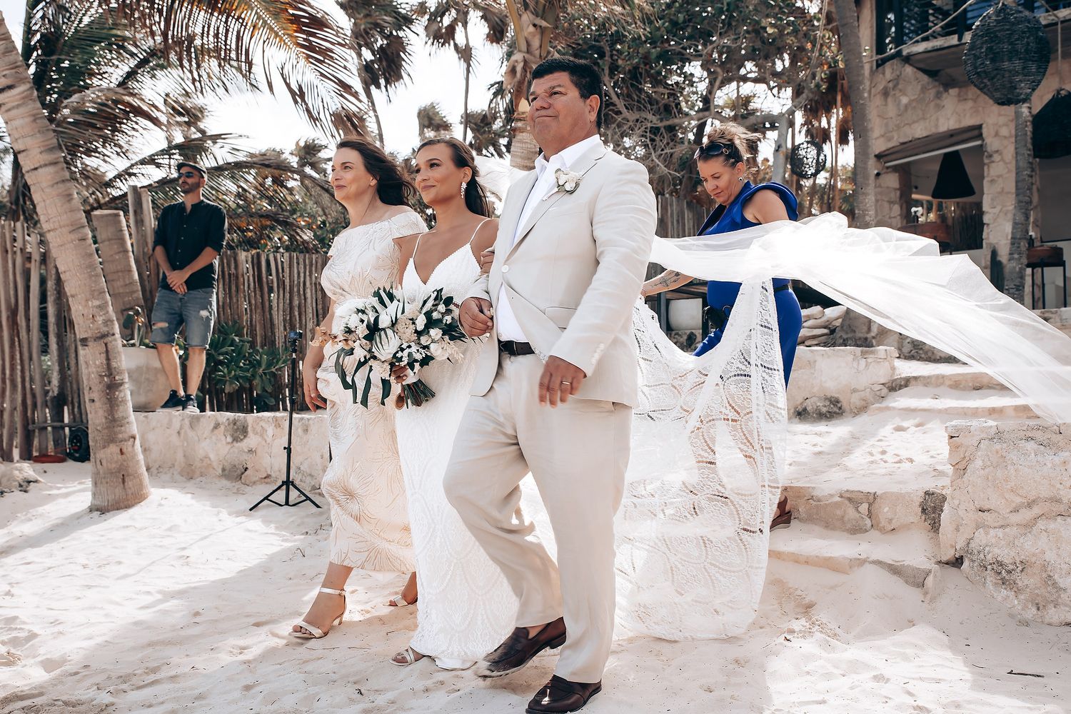 Newlyweds walking together at beachside venue with flowing white dress and palm trees.