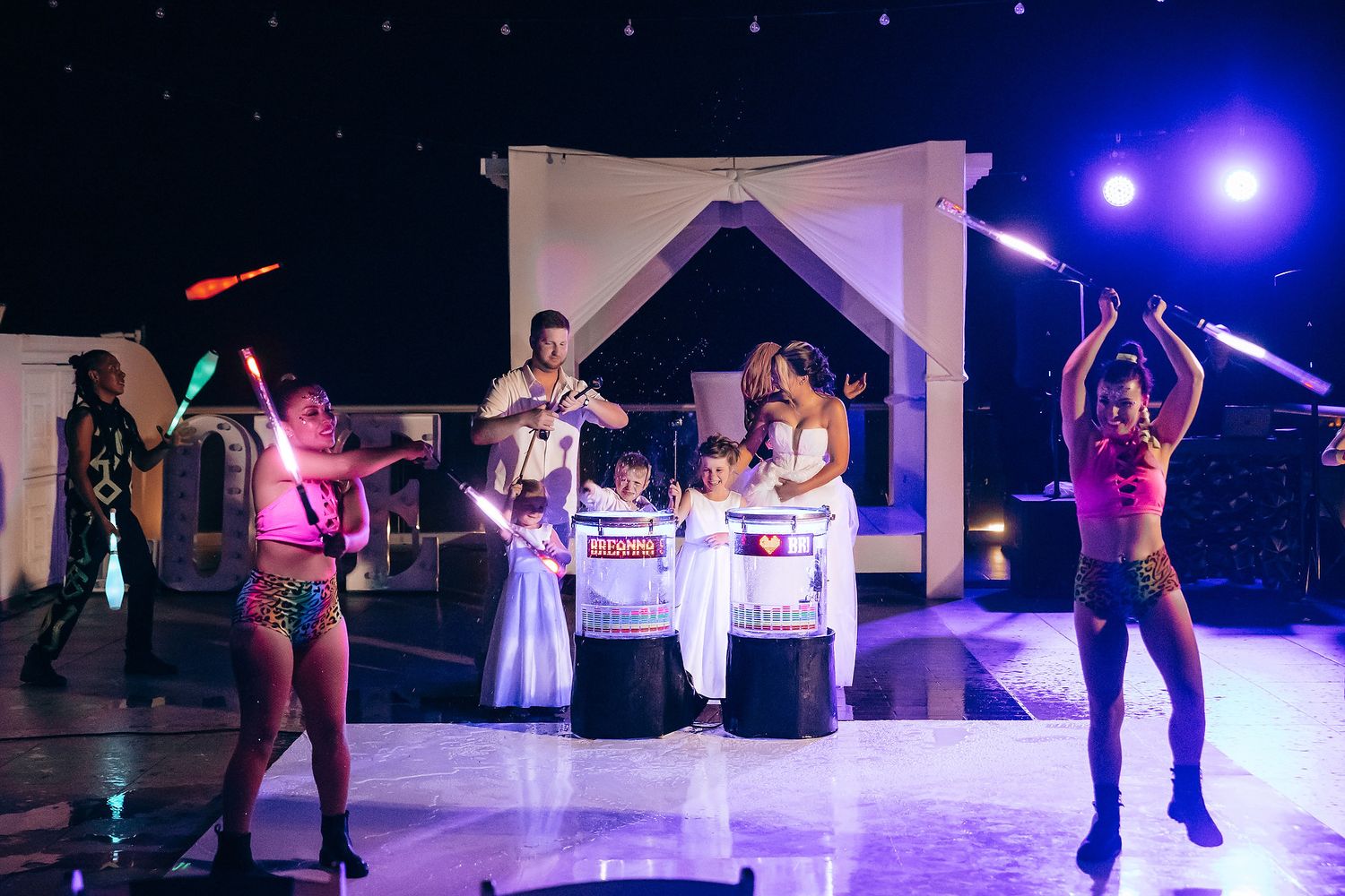 Colorful nighttime wedding reception with dancers performing under purple lighting.