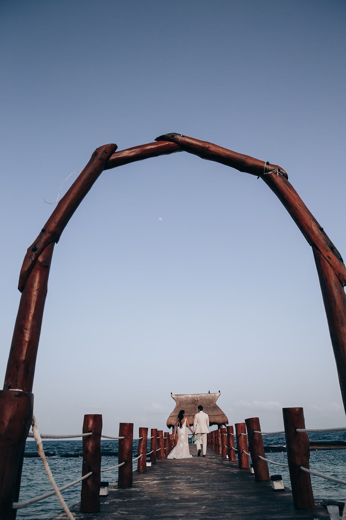 Dramatic wooden pier extending into blue ocean waters under clear sky.