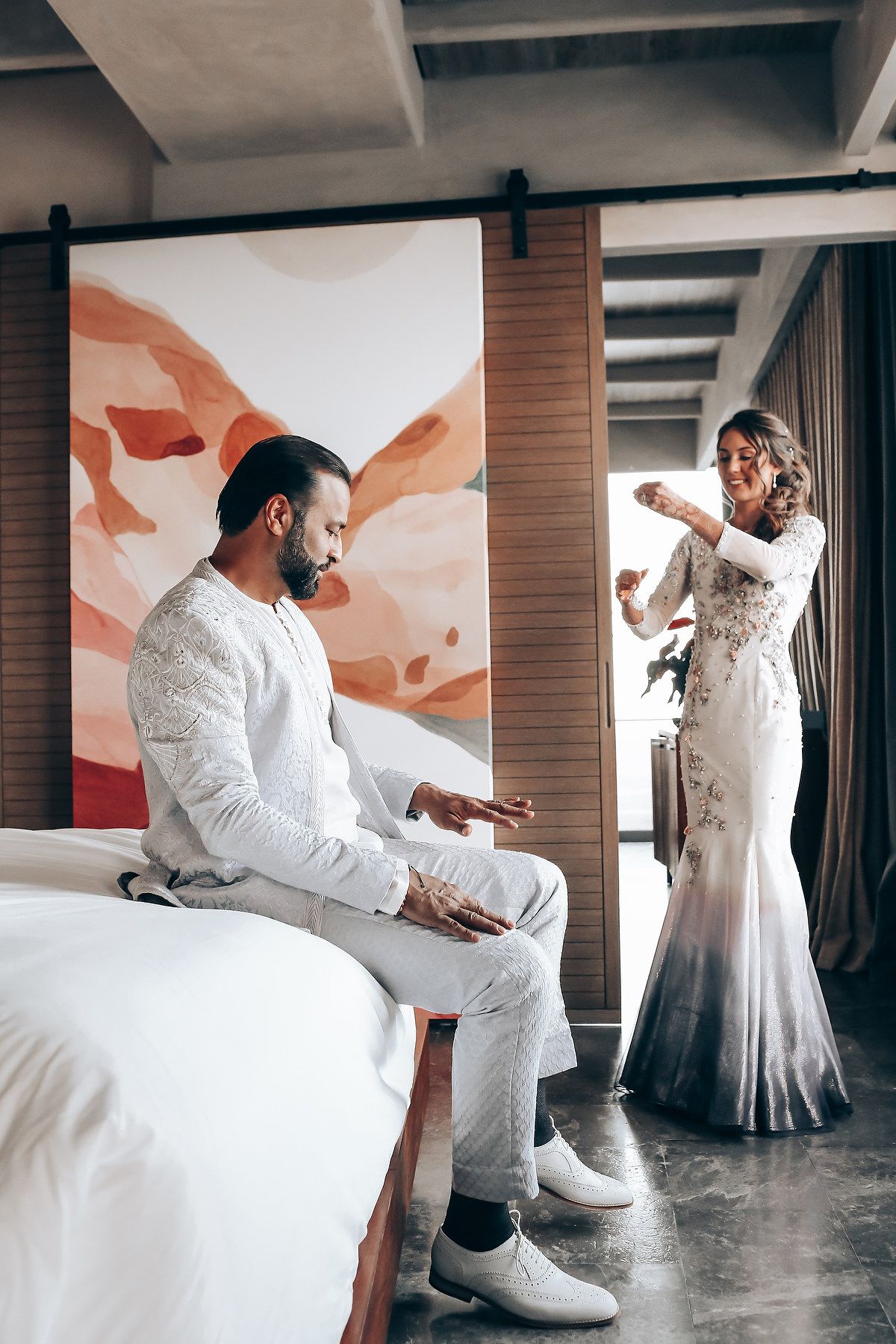 A sequence of dance movements captured in white outfits against an artistic wall with orange accents in an indoor space.