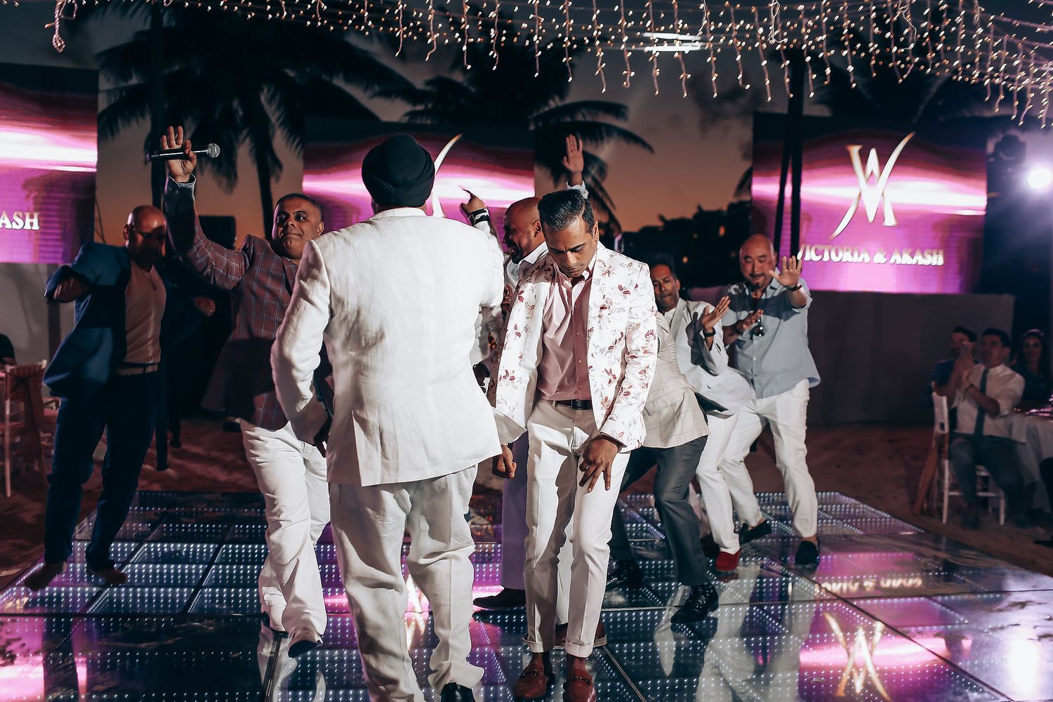People in white outfits dancing on an illuminated floor at an evening party with tropical decor.
