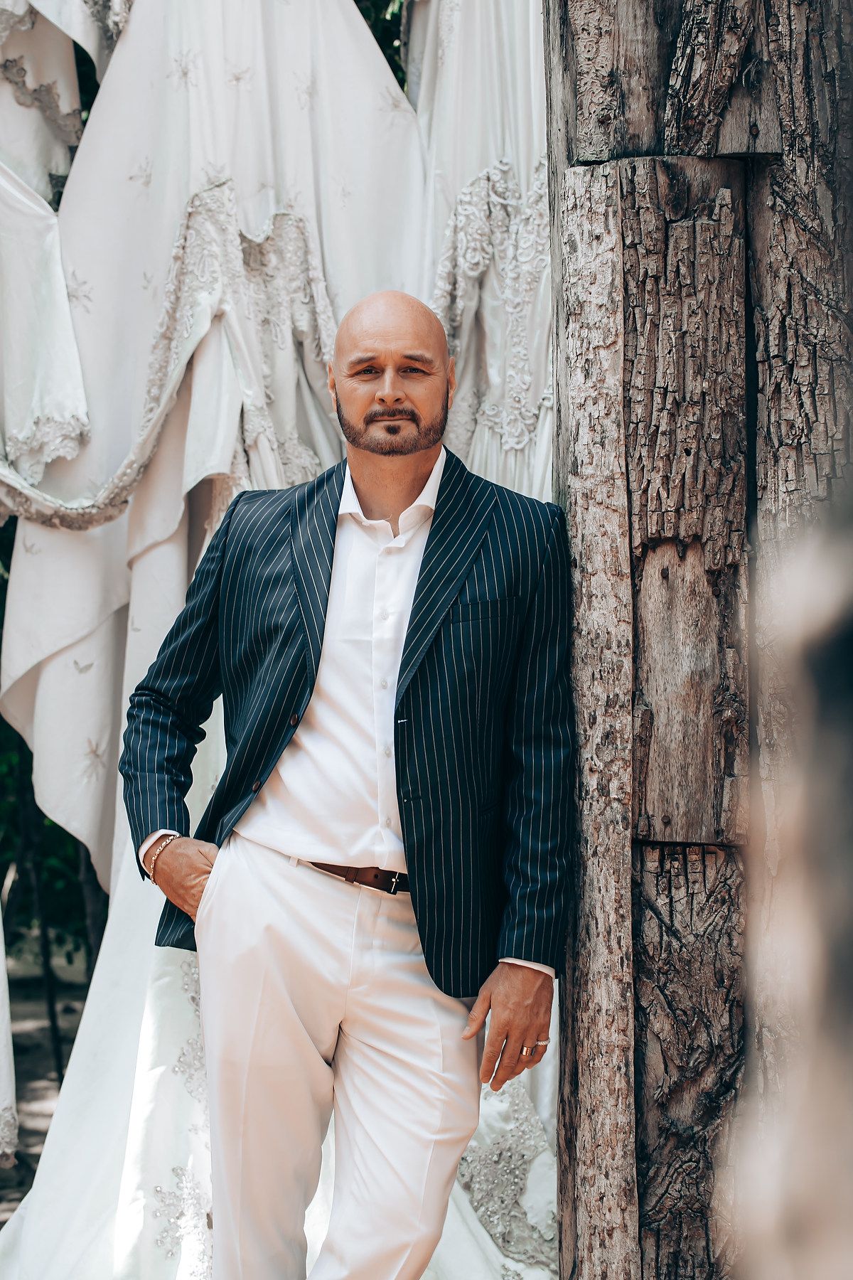 Elegant navy pinstripe blazer paired with white pants and shirt against backdrop of wedding dresses and rustic wood.