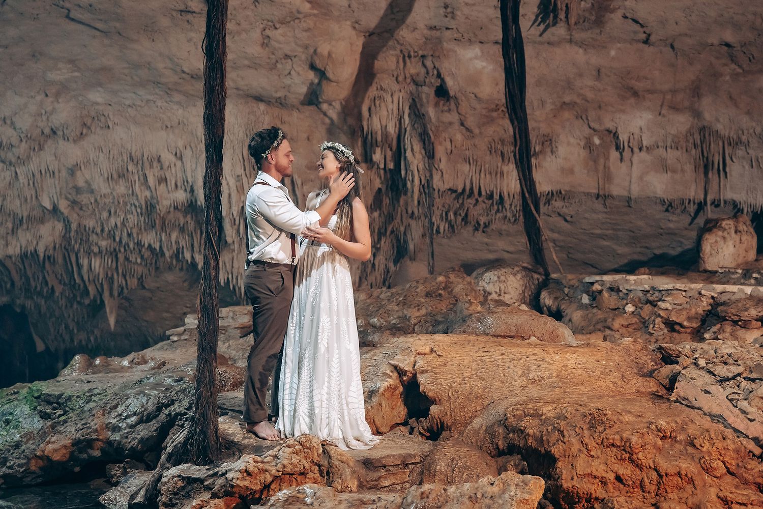 An intimate cave wedding ceremony with white dress against rustic rock walls and natural cave formations.