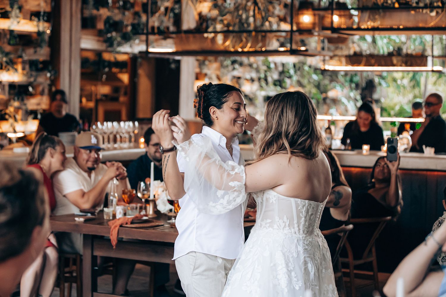 Guests celebrate and dance during a lively wedding reception at an elegant indoor venue with warm lighting.
