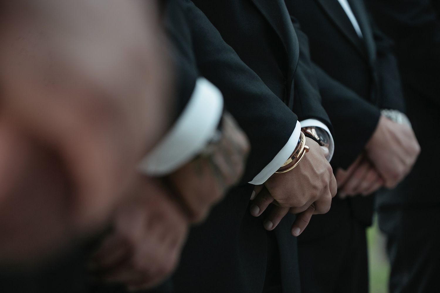 Close-up detail of hands and formal attire during an outdoor wedding ceremony.