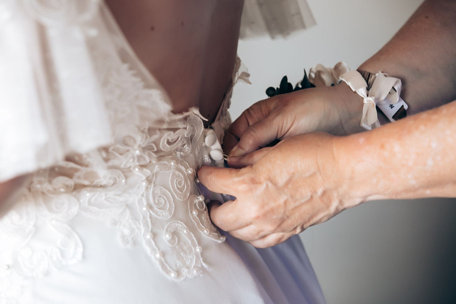 Close-up shots of hands adjusting and fastening a delicate white lace wedding dress.