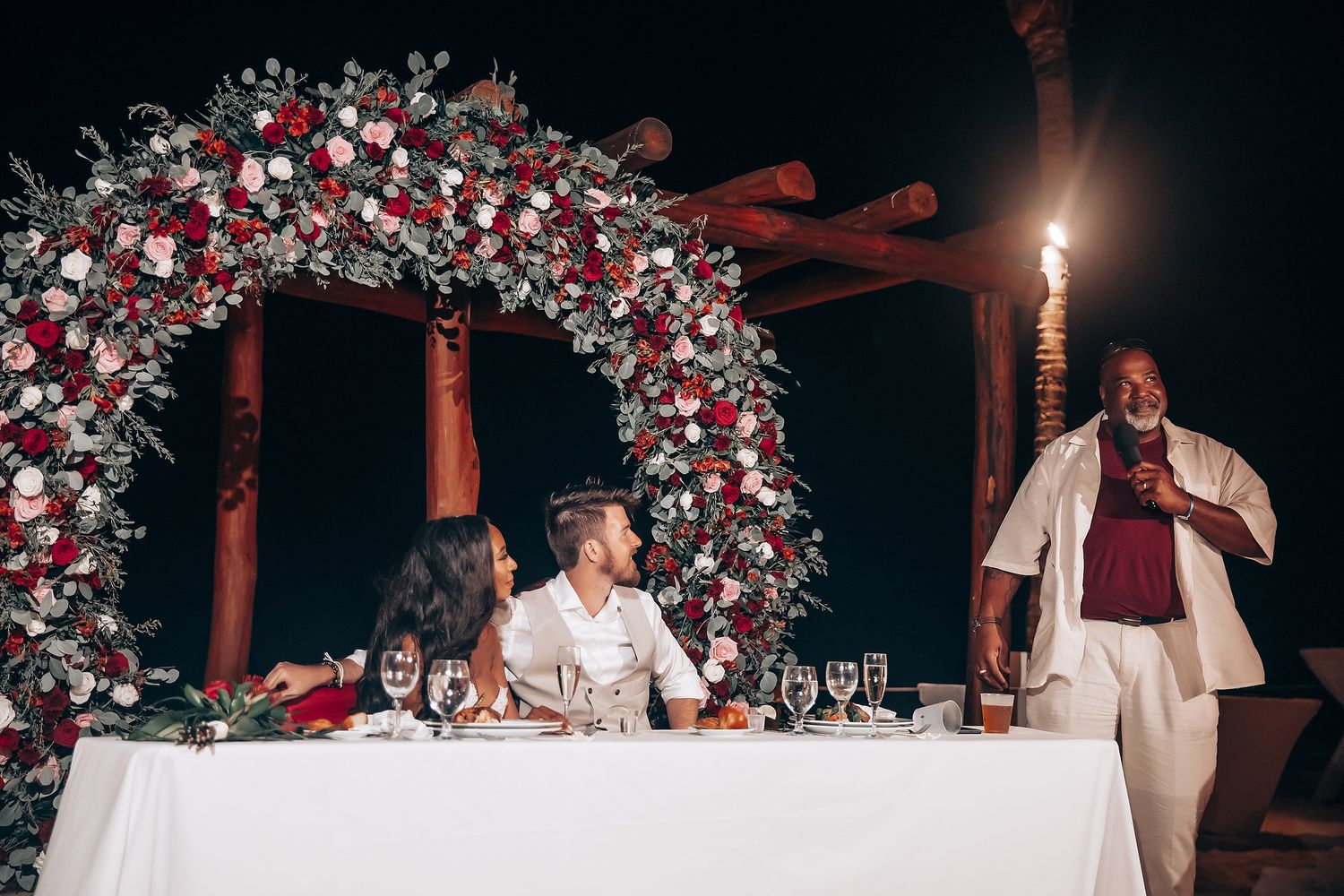 Wedding reception arch decorated with red and white flowers under evening lighting.