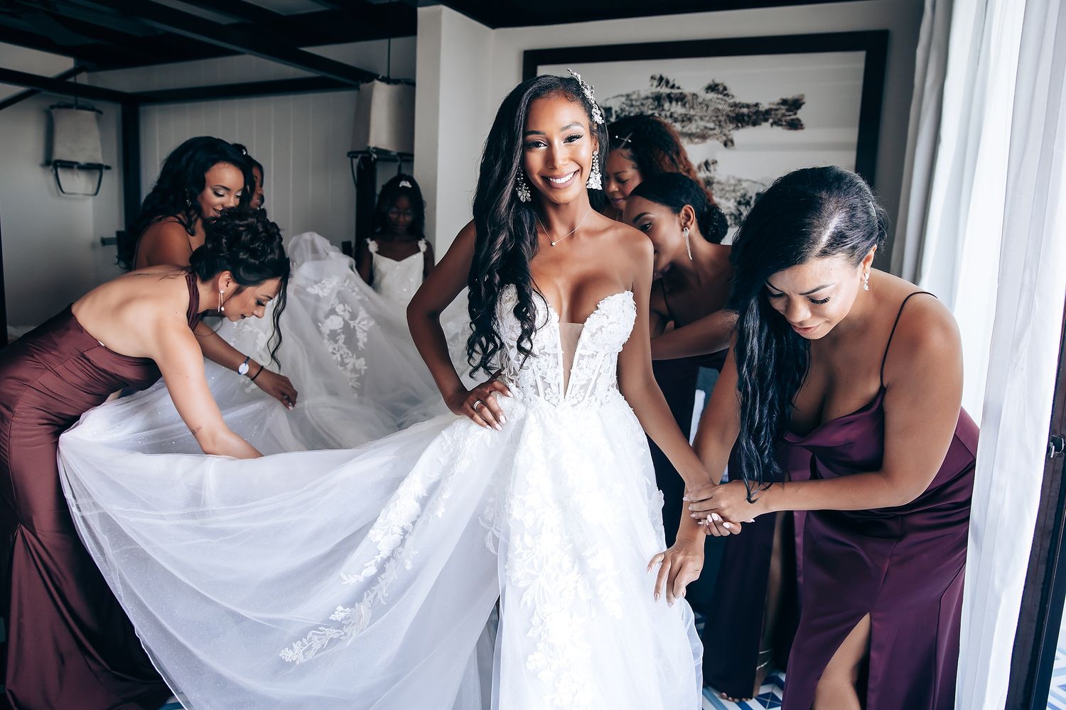Wedding party members assisting with bridal preparations in a sunlit room.