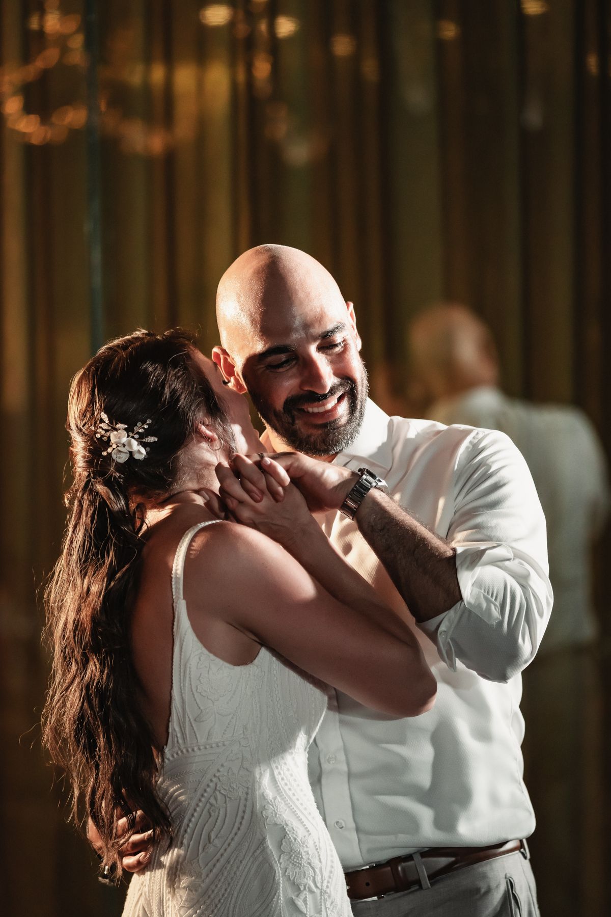 Bald groom smiling tenderly while dancing with bride in white dress during romantic wedding first dance.