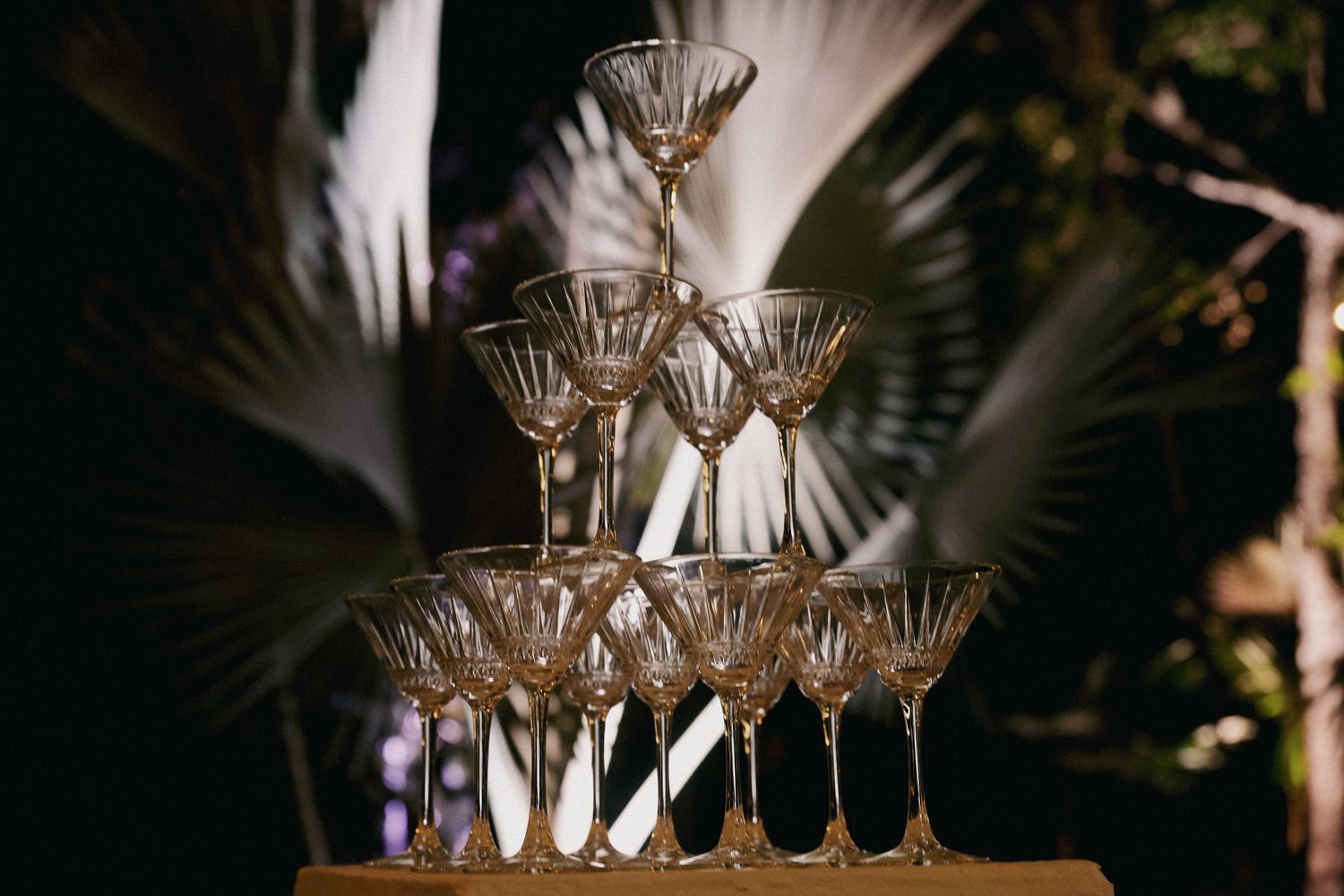 Elegant champagne tower with crystal coupe glasses stacked in pyramid formation at an outdoor evening event.