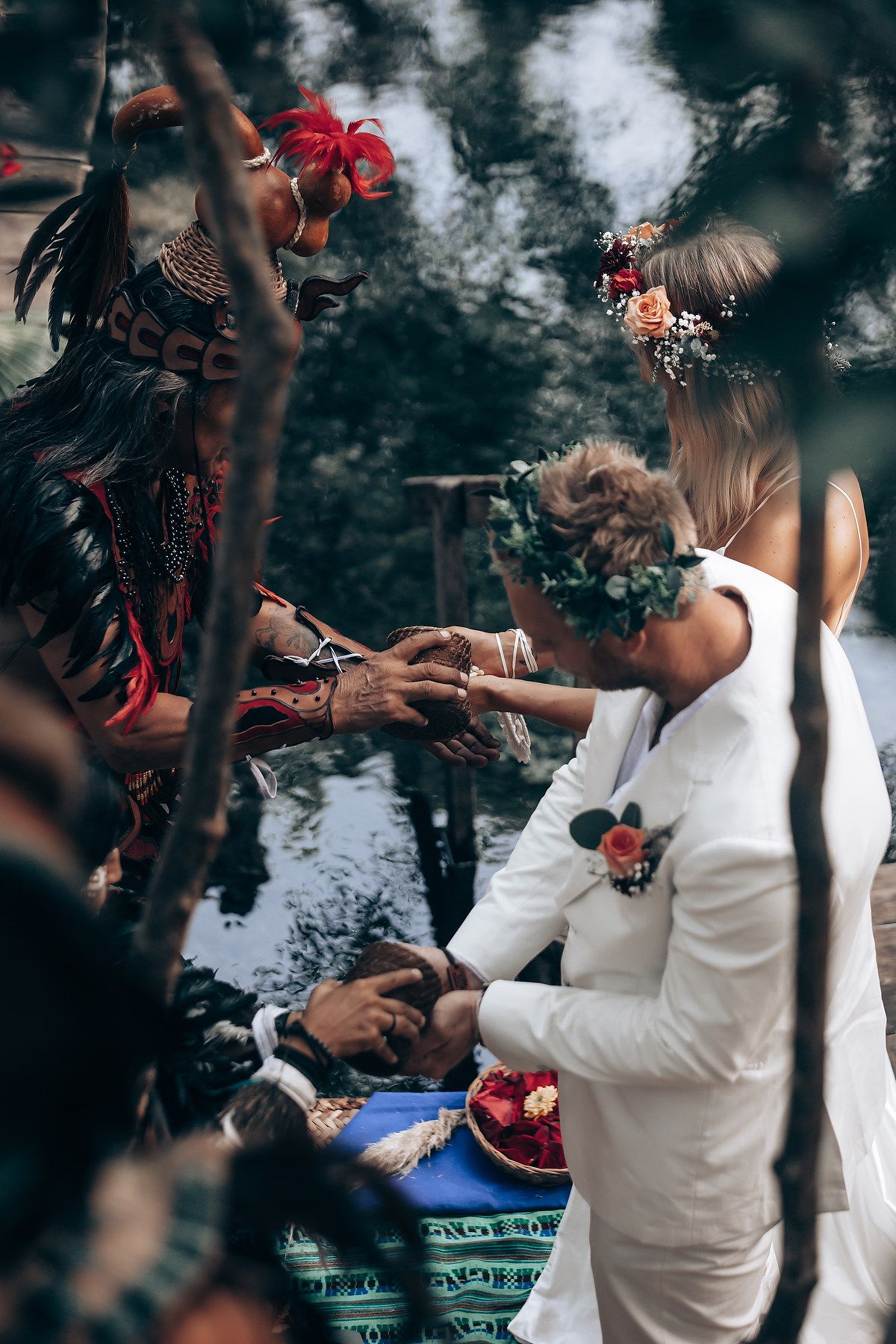 Couple participates in traditional handfasting ceremony with red ribbons in outdoor woodland setting.