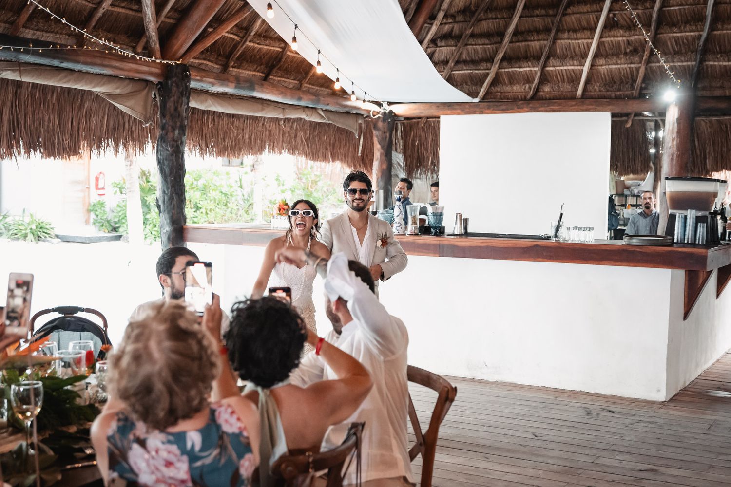 Newlyweds make joyful grand entrance at tropical beach wedding reception with cheering guests.