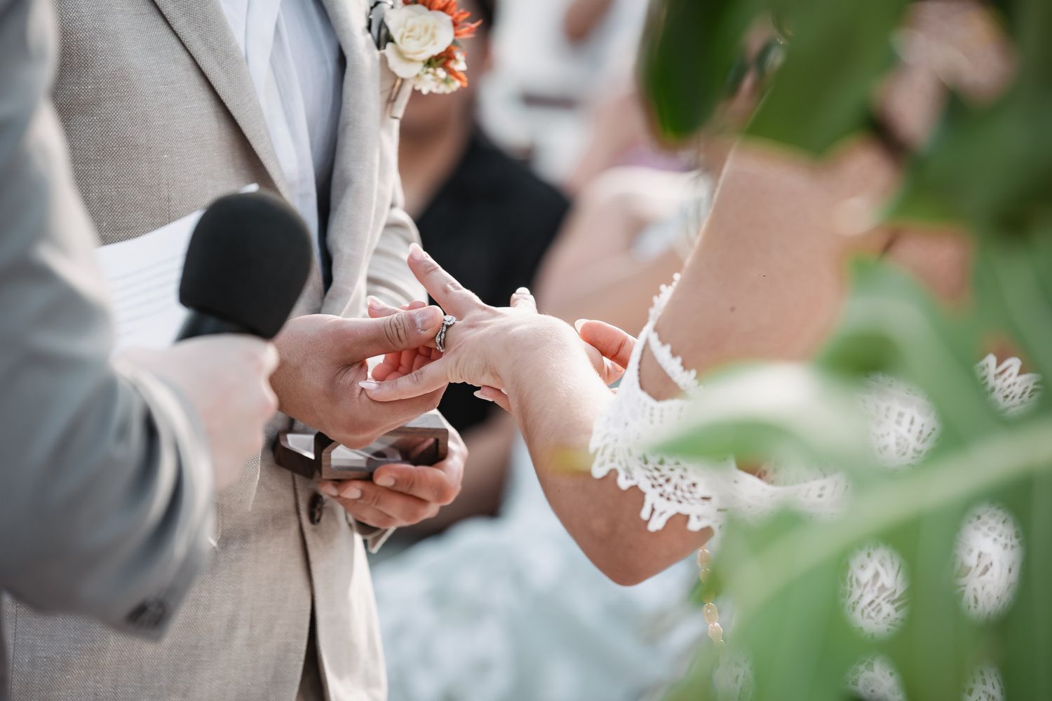 Groom placing wedding ring on bride's finger during outdoor ceremony.