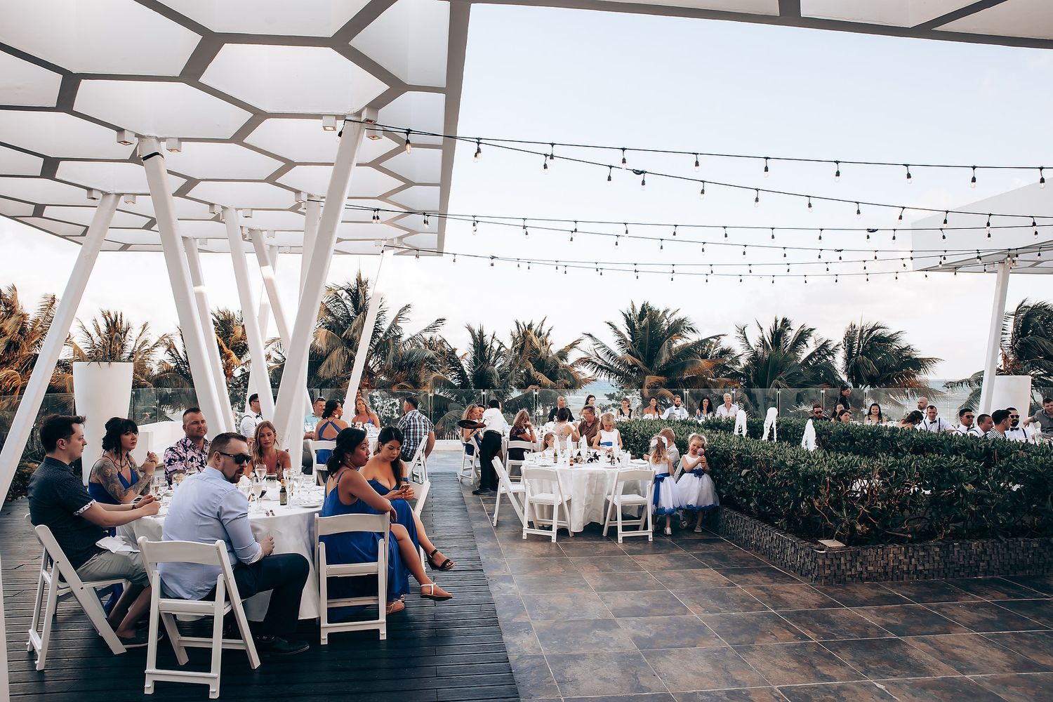 Reception setup with white chairs and string lights under a geometric canopy.