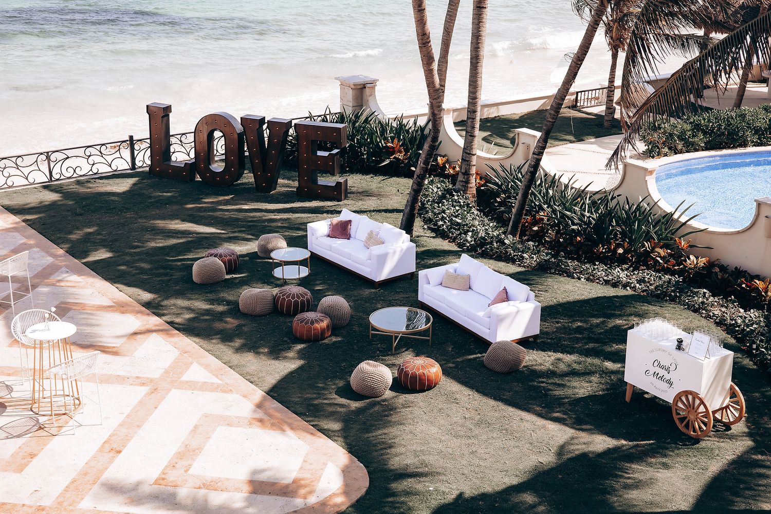 Outdoor wedding reception setup with rustic decor and seating under palm trees.