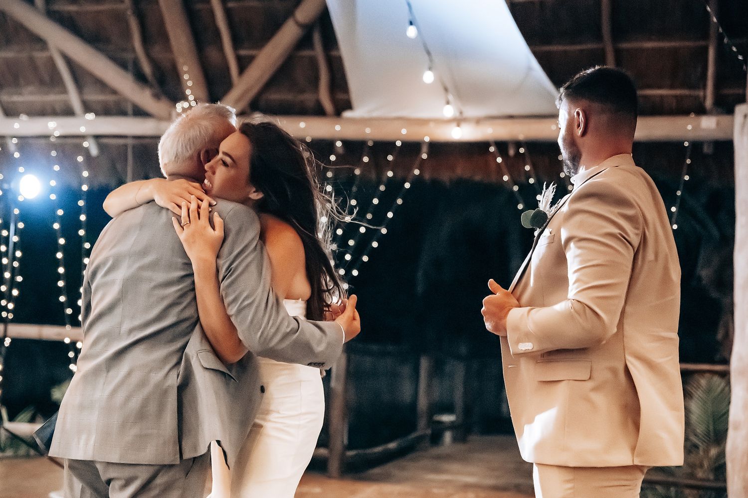 Romantic couples dancing together at an elegant indoor wedding reception with twinkling string lights in the background.