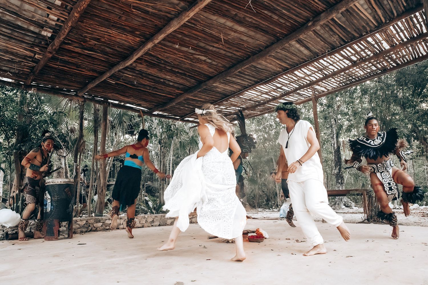 People dancing and celebrating at an outdoor covered venue with musicians performing live music in a tropical setting.