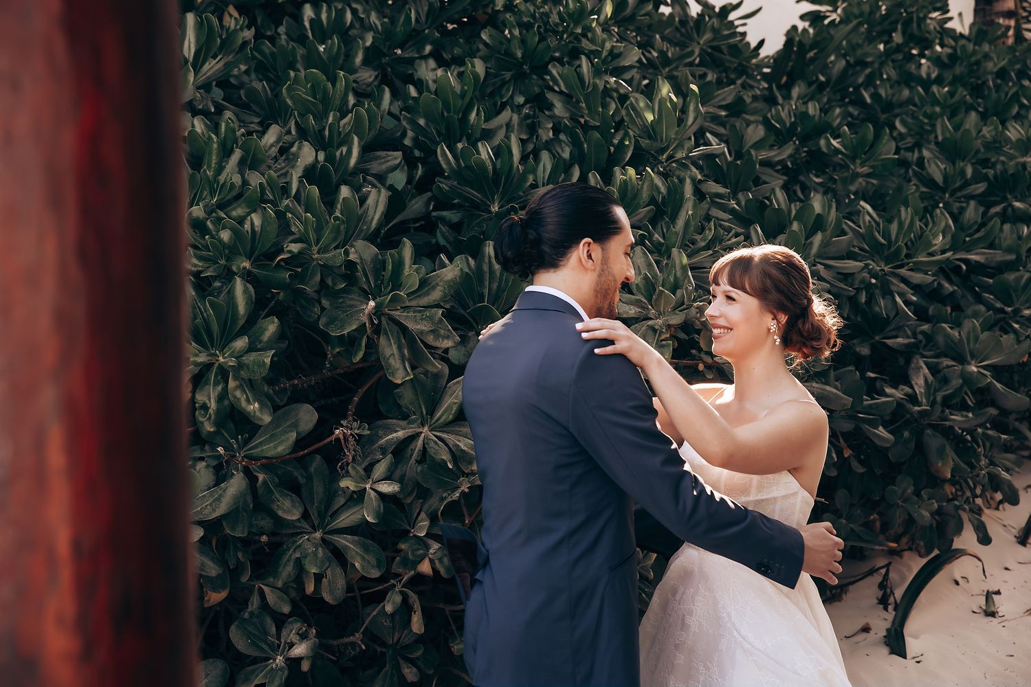 Wedding ceremony setup with greenery and wooden pillars in a tropical garden setting.