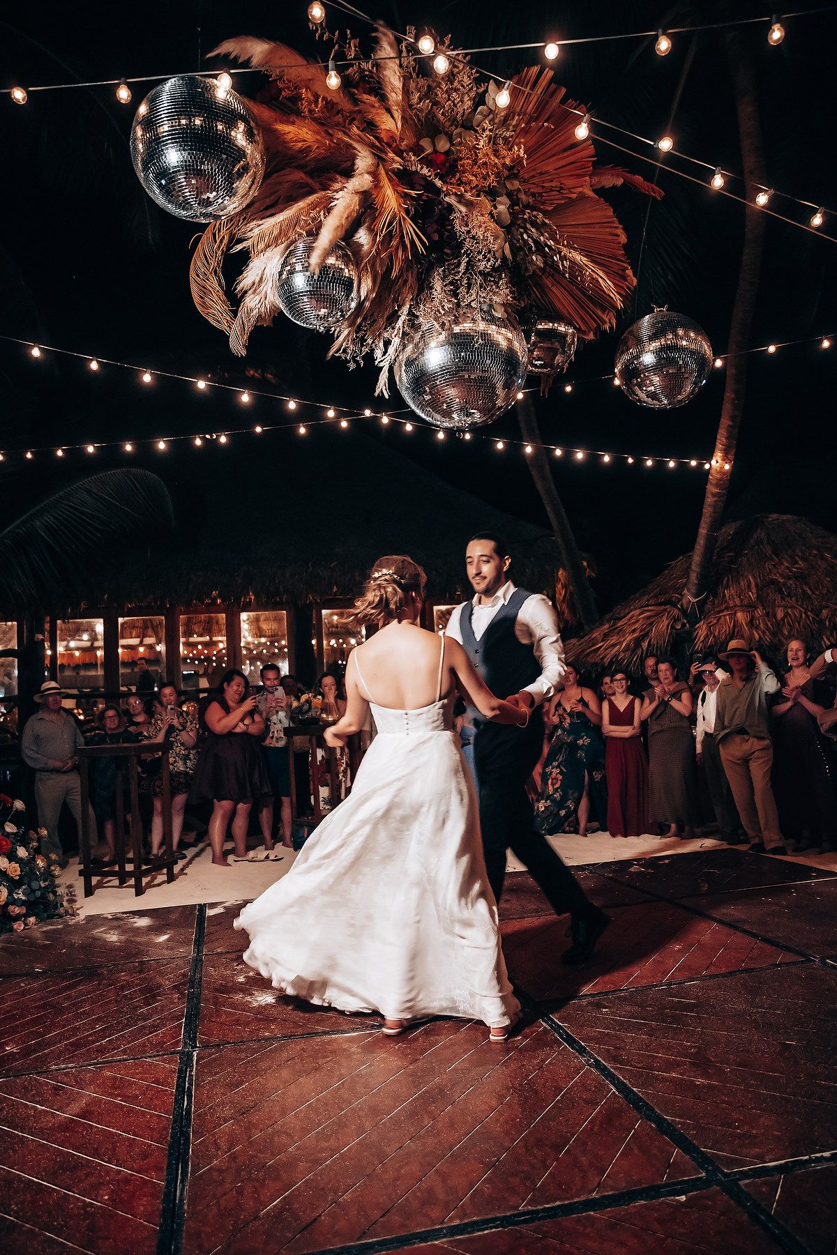 Wedding reception dance floor under string lights and disco balls with guests watching.
