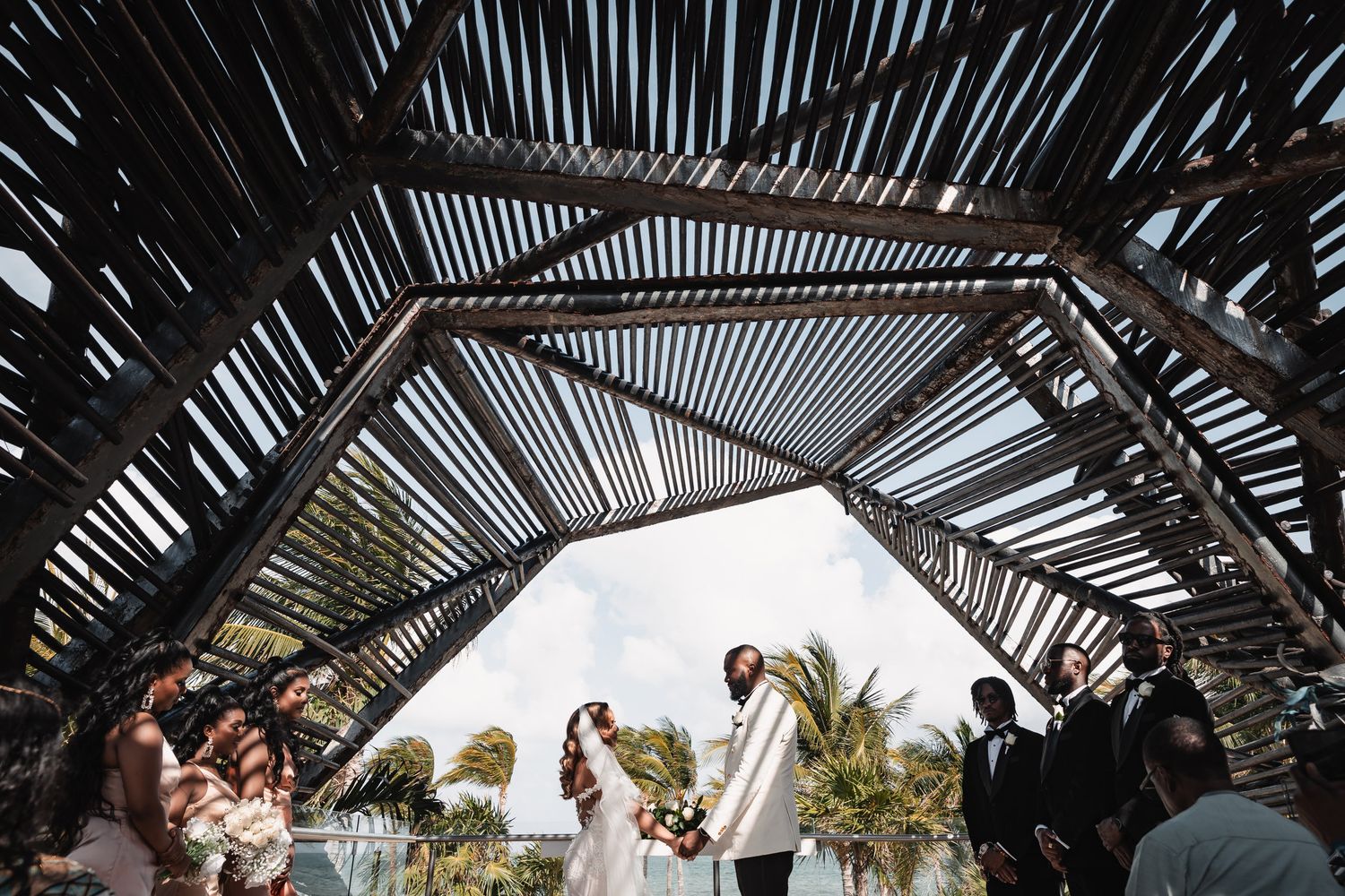 Wide-angle view of wedding ceremony under dramatic rustic bamboo pergola structure.