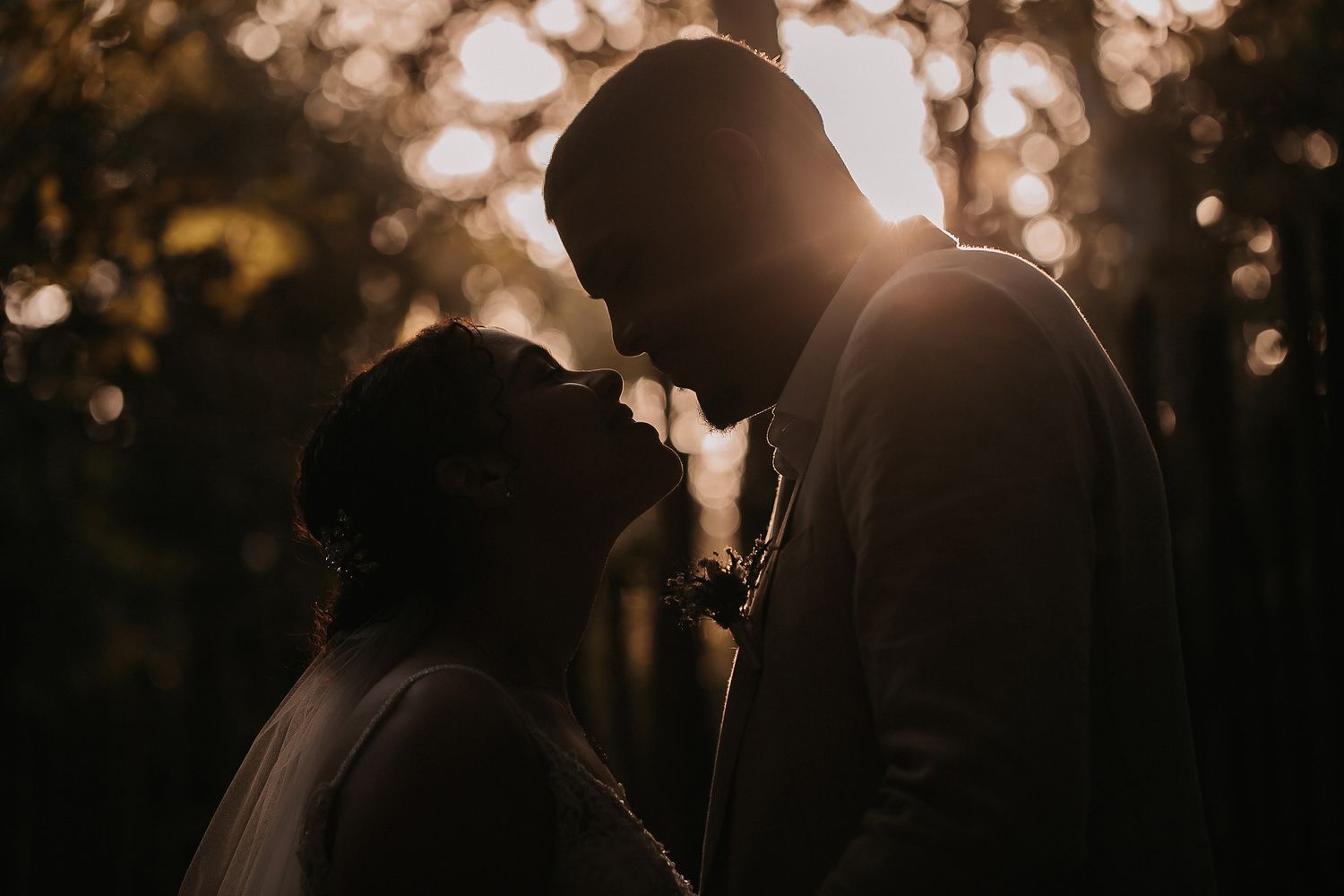 Silhouette of a wedding couple against a glowing sunset through trees.