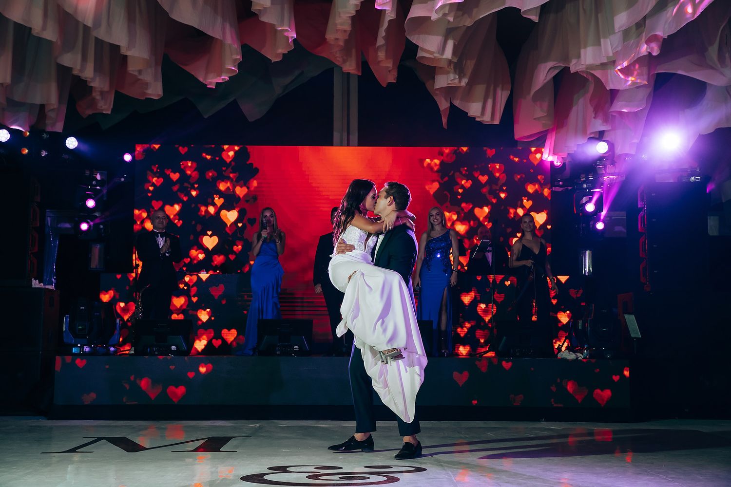 Wedding reception dance floor with dramatic red lighting and heart projections.