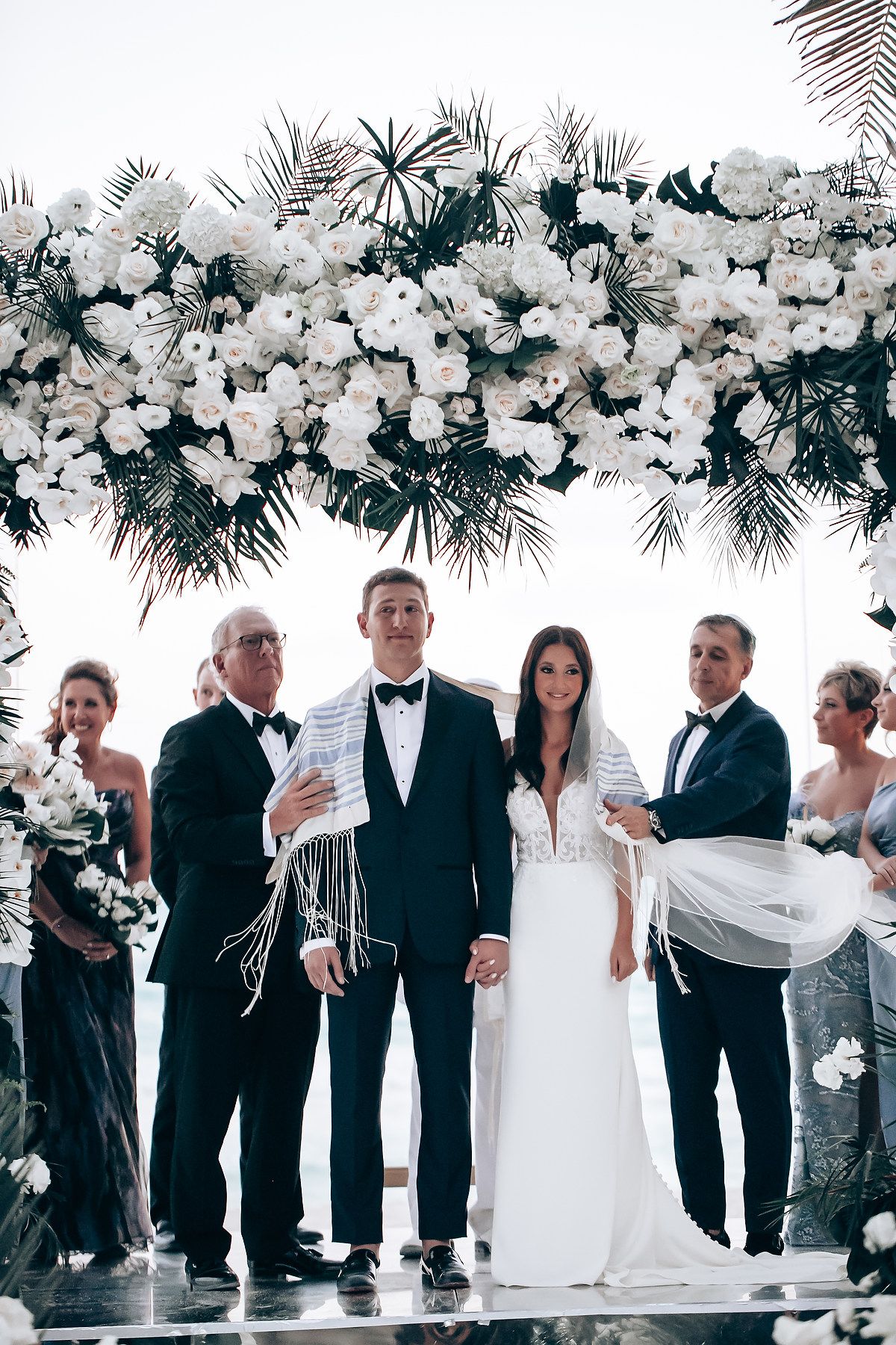 Wedding ceremony setup with luxurious white floral canopy and tropical palm decor.