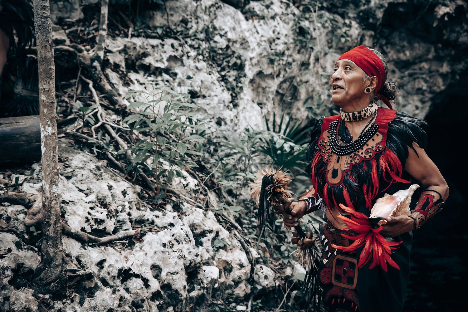 Couple in traditional attire performs a spiritual ceremony in a natural cave setting with red accents.