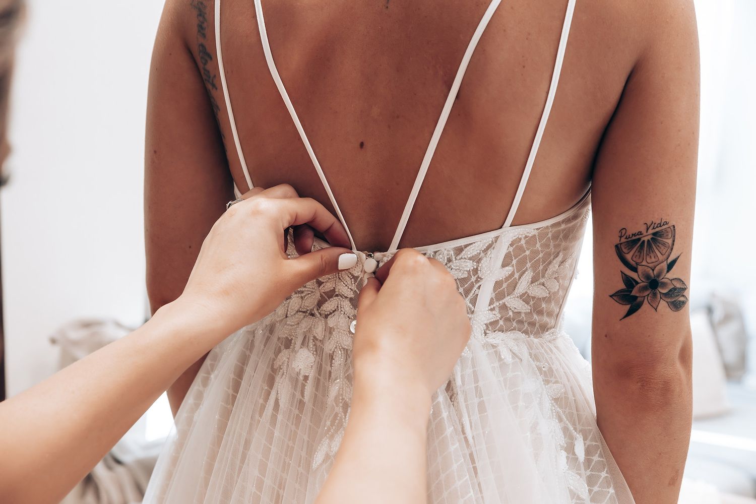 Close-up details of a white lace wedding dress with delicate straps and visible tattoo artwork.