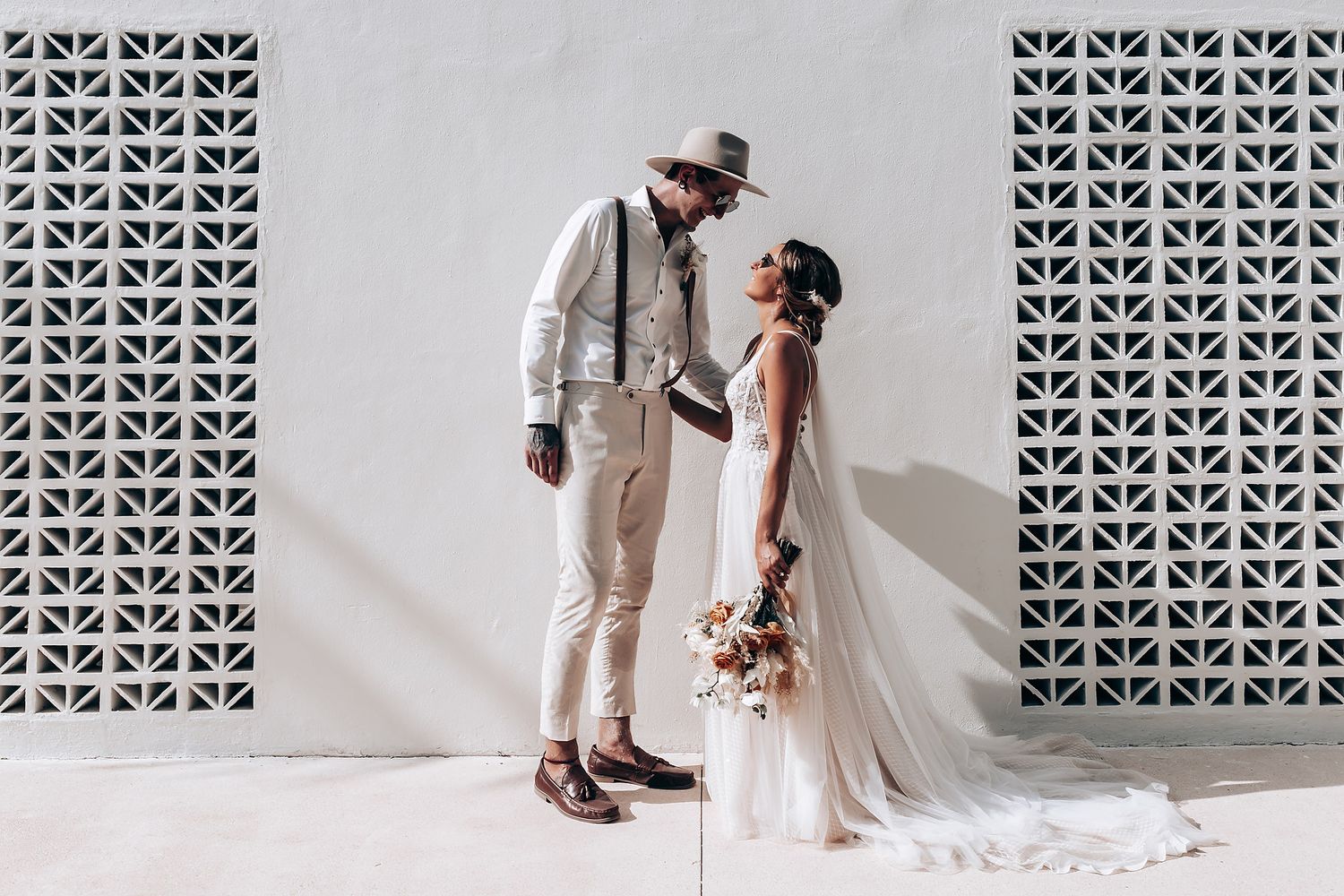 Wedding couple posing against decorative white wall with geometric patterns.