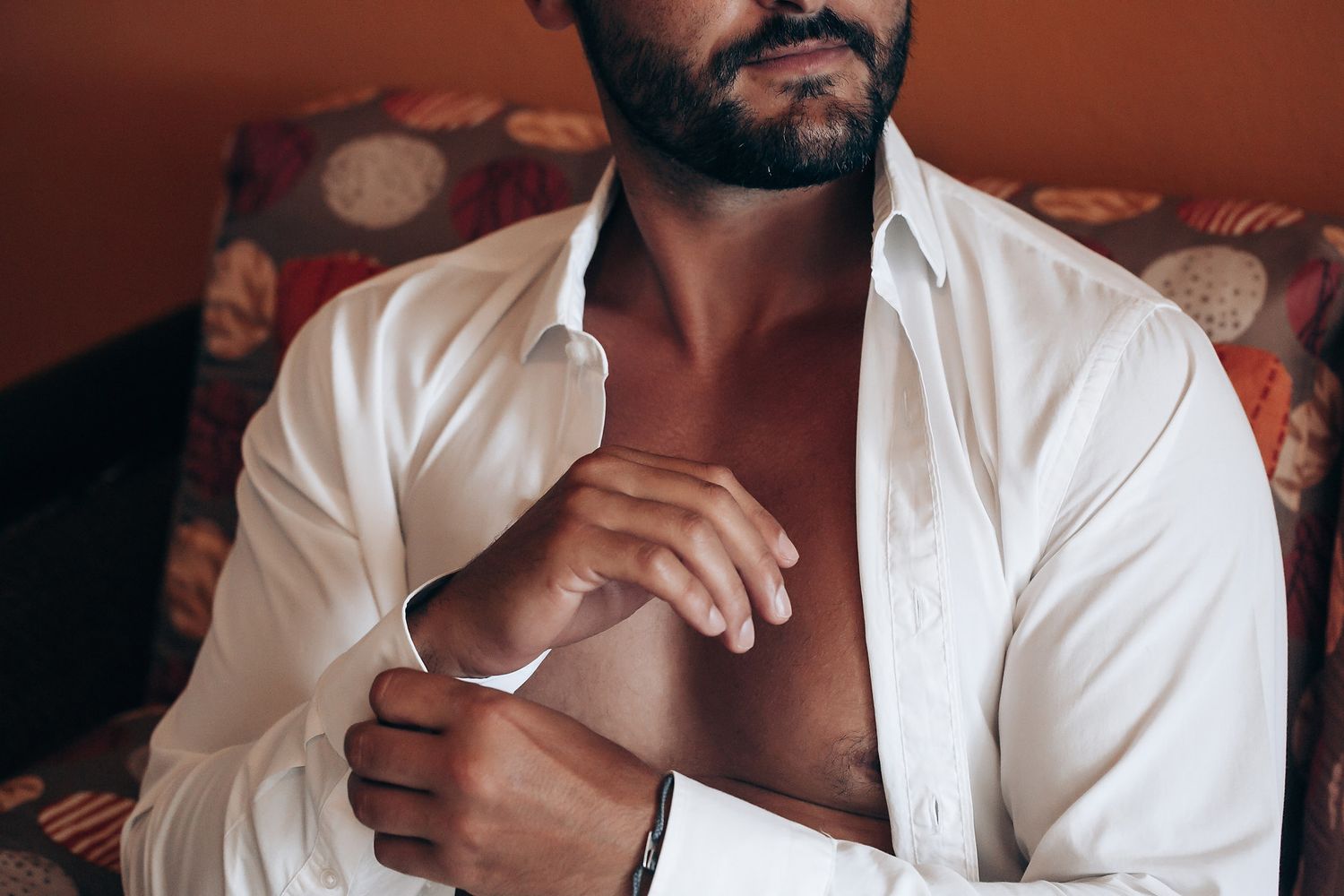 A person wearing a crisp white dress shirt adjusts their collar in a warm-toned indoor setting.