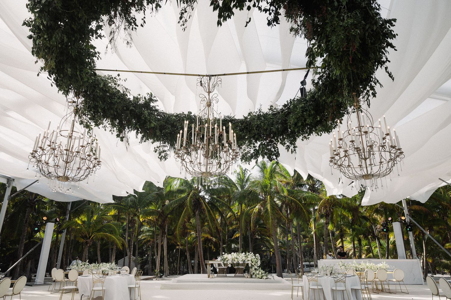 Elegant wedding reception tent with crystal chandeliers and lush greenery floral installations.