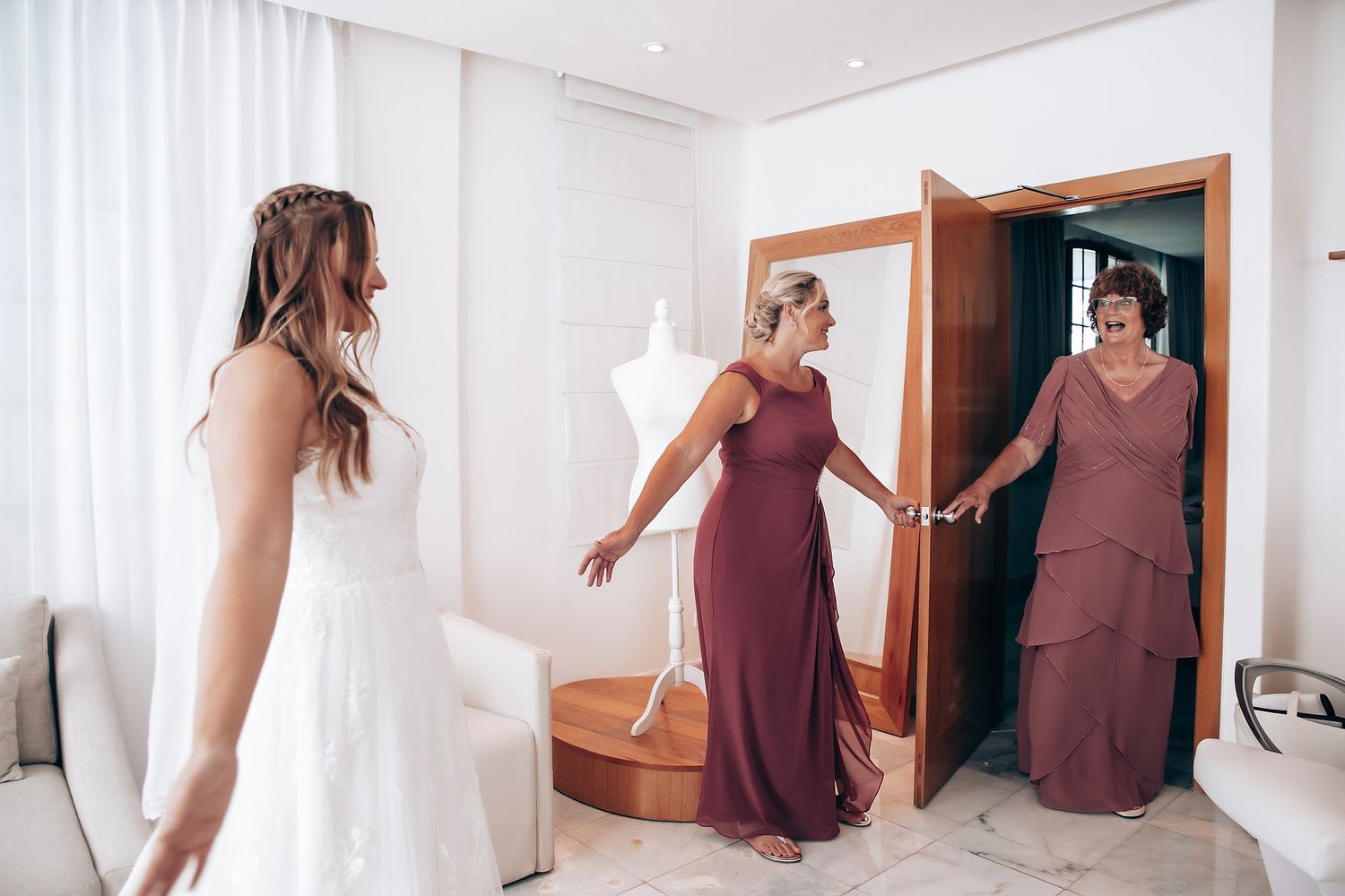 Multiple shots of people in burgundy bridesmaid dresses helping with wedding preparations in a bright room.