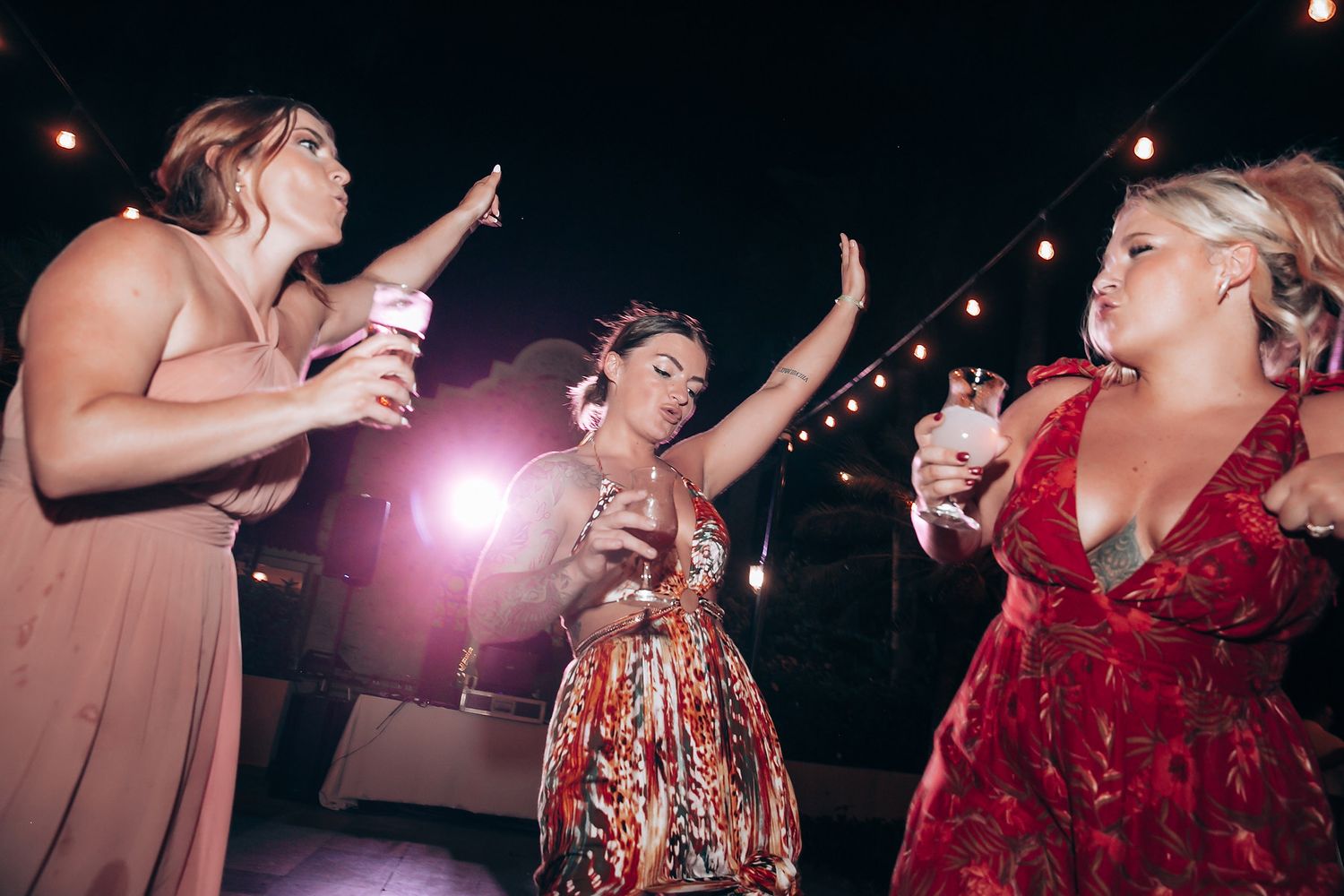 Party guests dancing and celebrating under string lights at an evening outdoor reception.