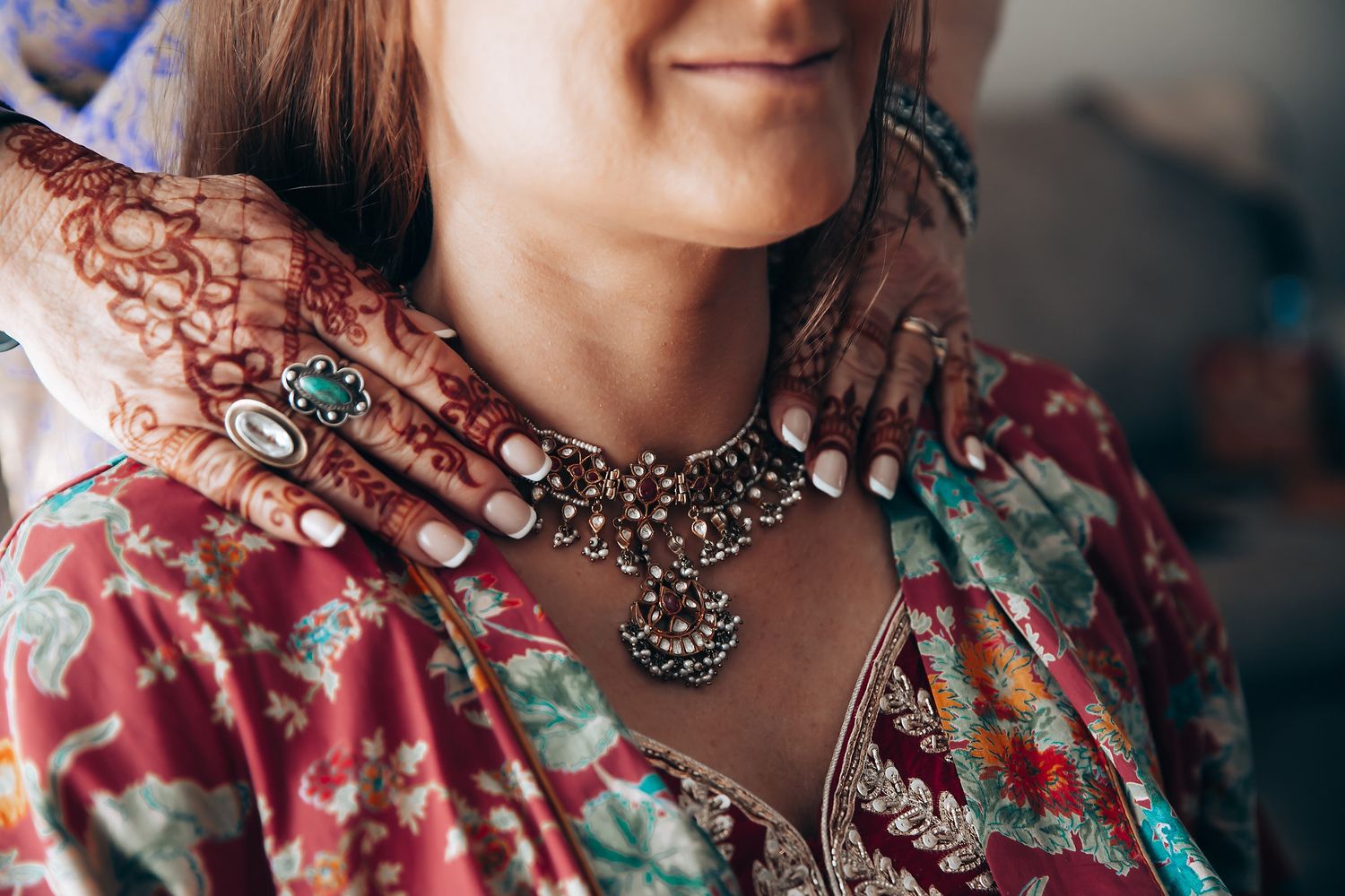 Close-up of ornate bridal jewelry and henna-decorated hands against a floral patterned dress.