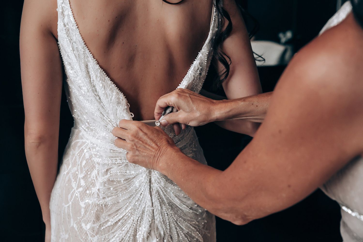 A close-up series of hands adjusting a white lace wedding dress on the back.