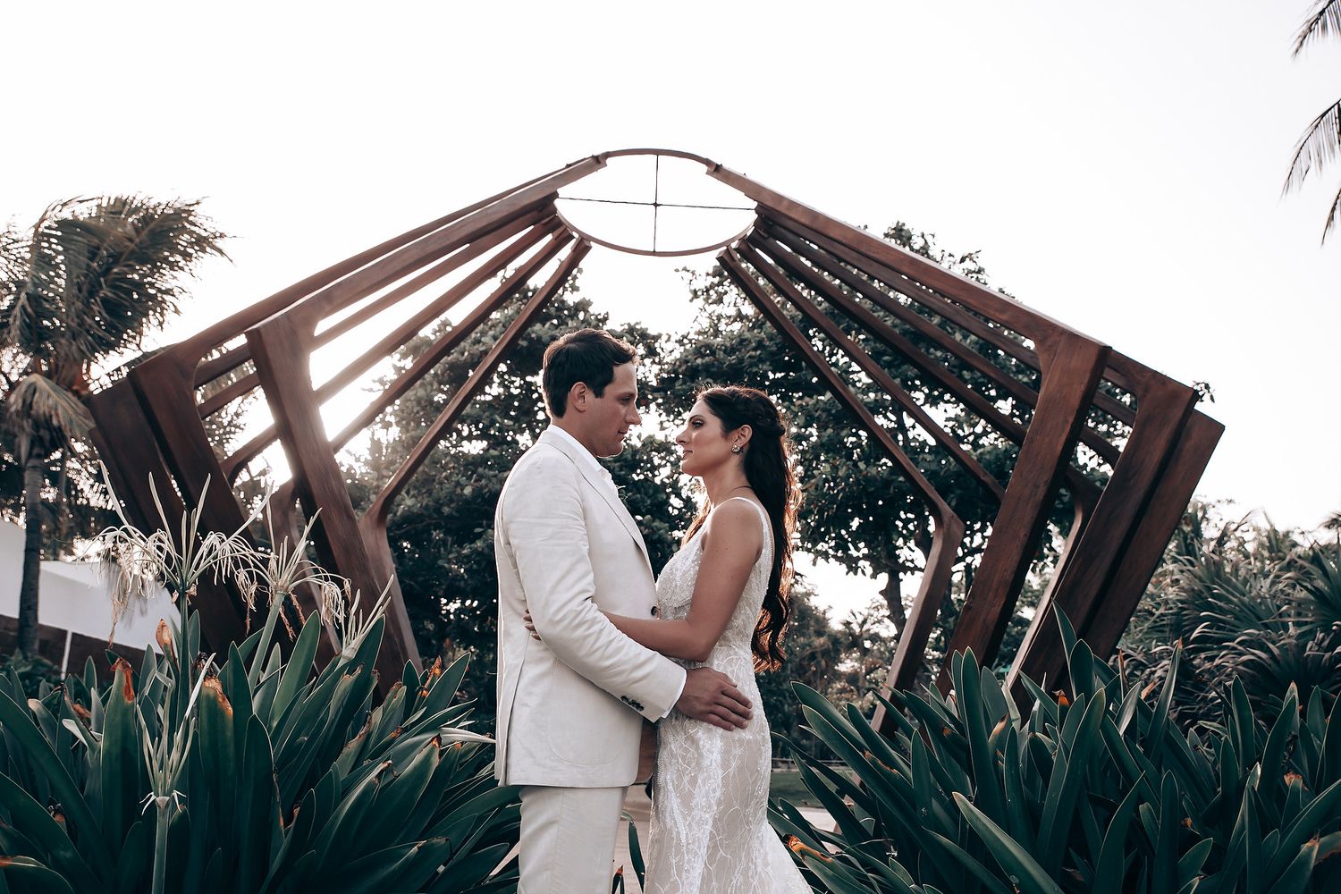 Romantic outdoor wedding ceremony with tropical greenery and wooden arch structure.