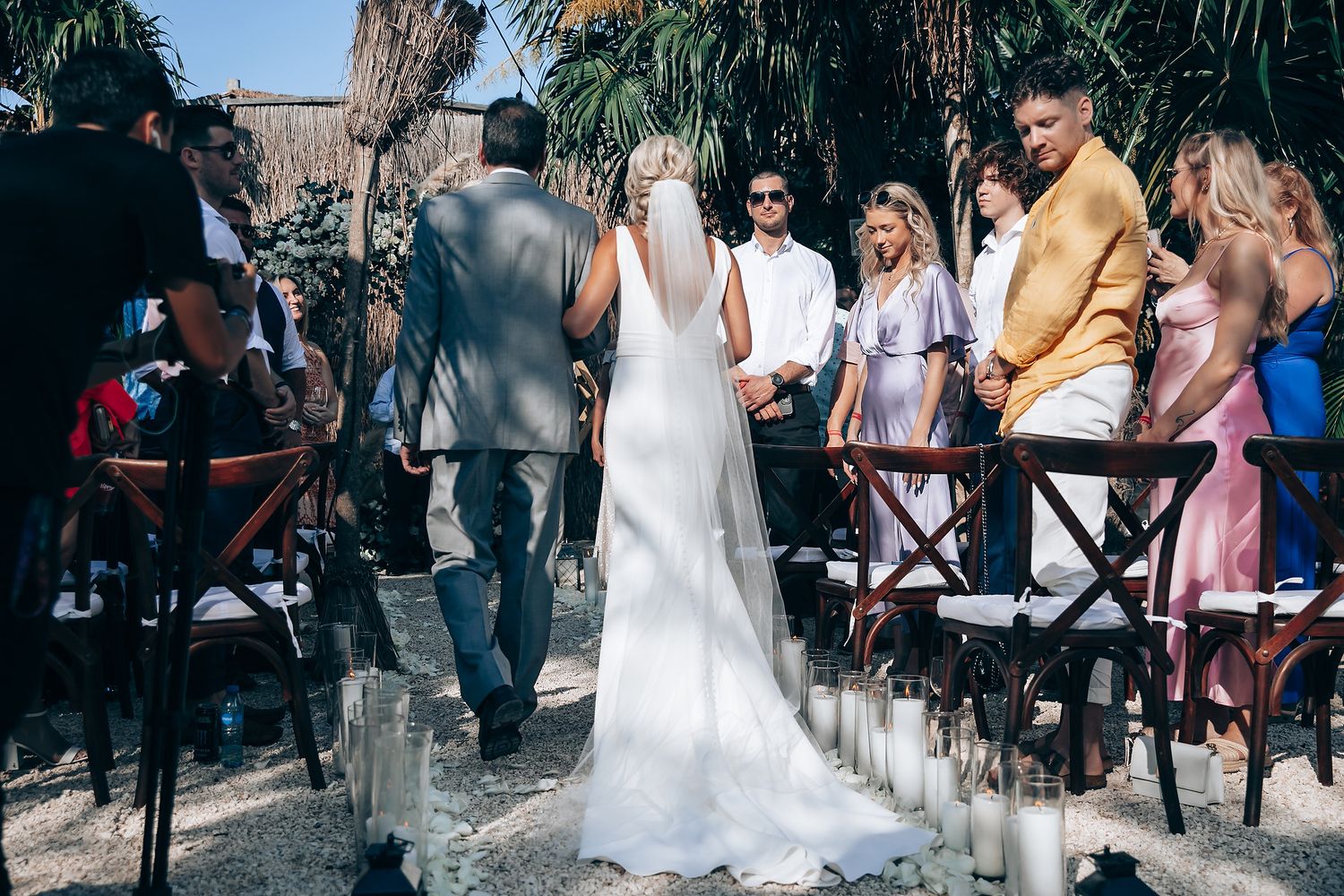 Wedding celebration in a tropical garden setting with guests seated on wooden chairs.