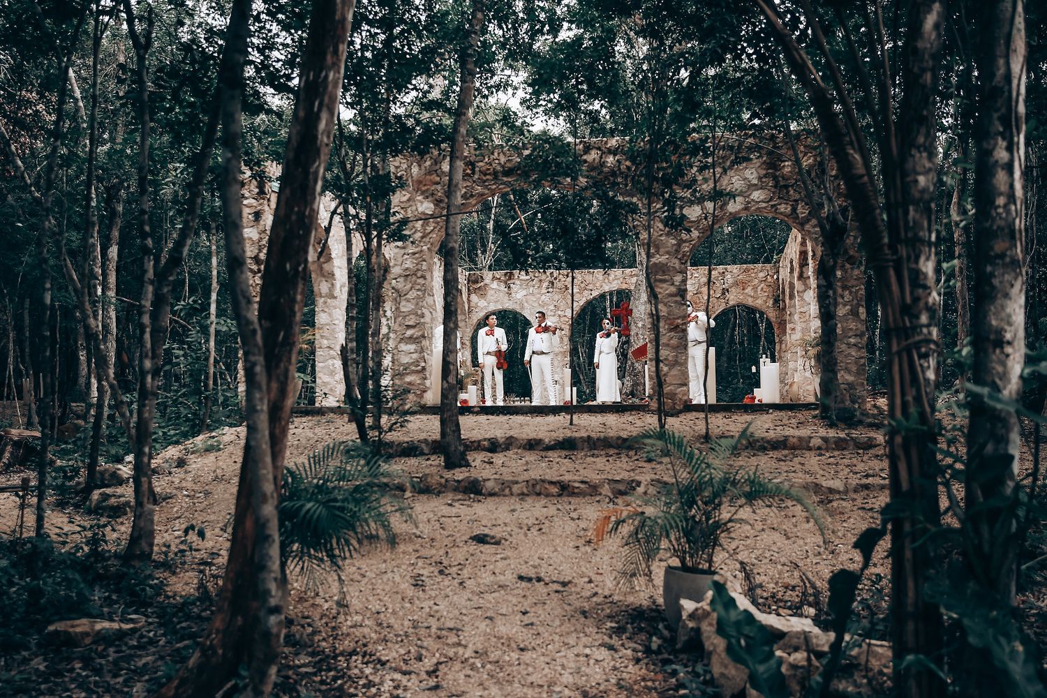 A silhouetted figure stands beneath stone archways of ancient ruins surrounded by a mystical forest setting.