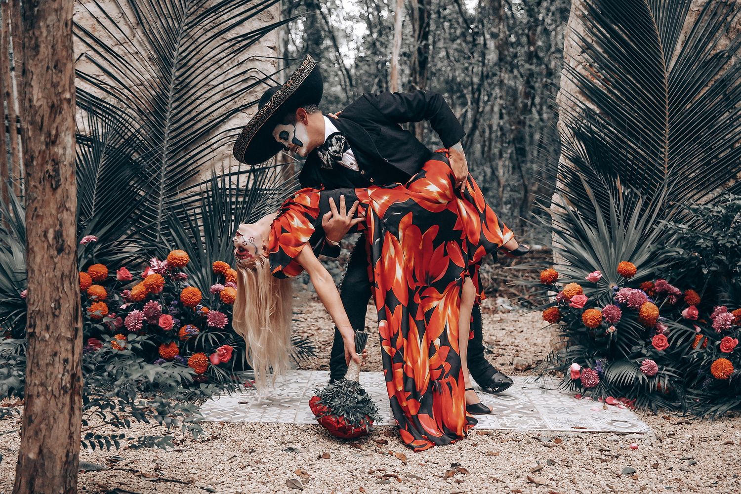 Group gathered in a garden setting with red floral decorations and palm fronds visible.