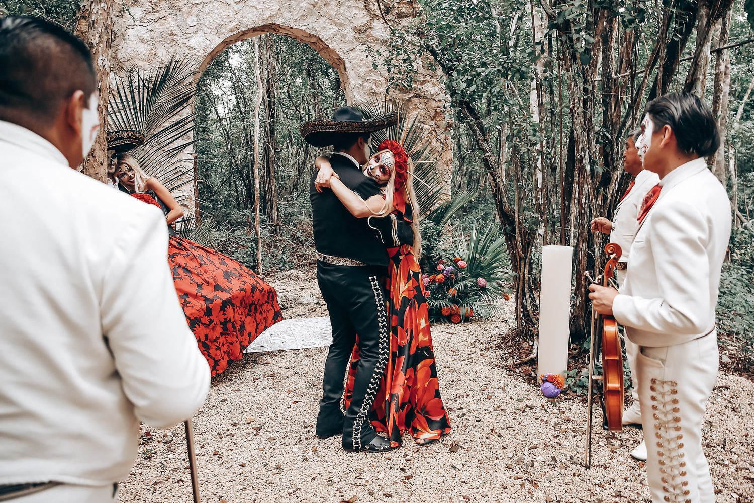 Dancers perform in an outdoor forest setting with one wearing a flowing red dress.