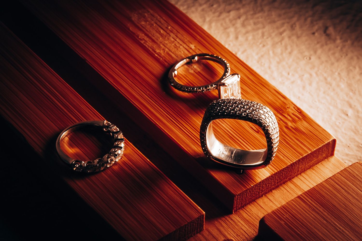 Wedding rings captured in dramatic lighting on a wooden surface with warm tones.