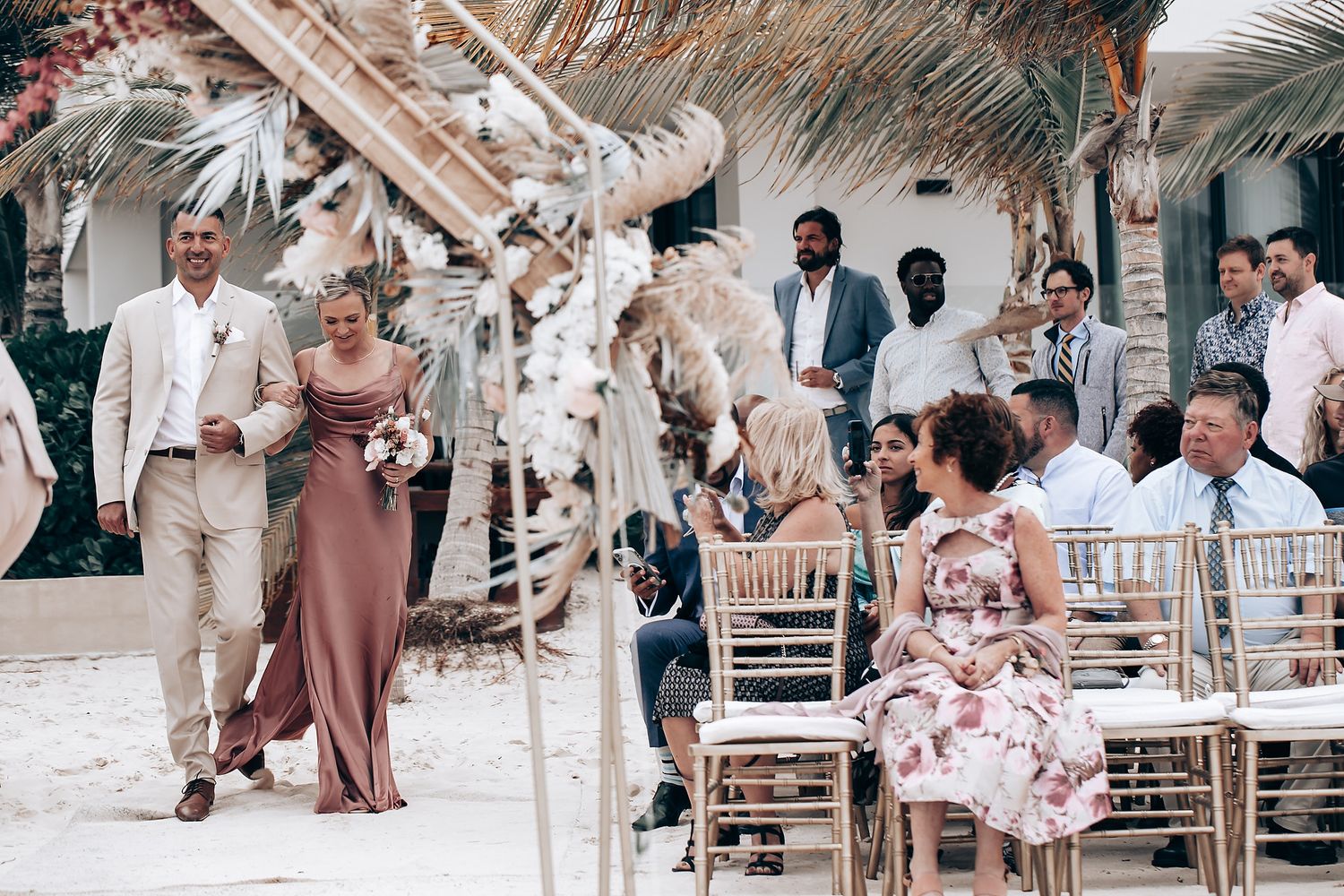 Wedding guests seated in white chairs at an elegant outdoor beachfront ceremony.