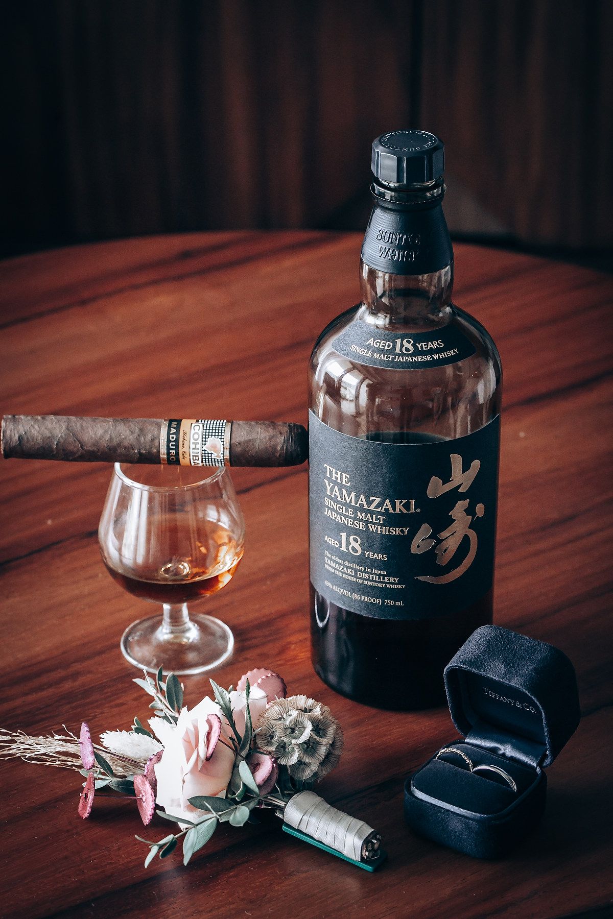 Yamazaki whiskey bottle and glass displayed on wooden table with delicate white flowers.