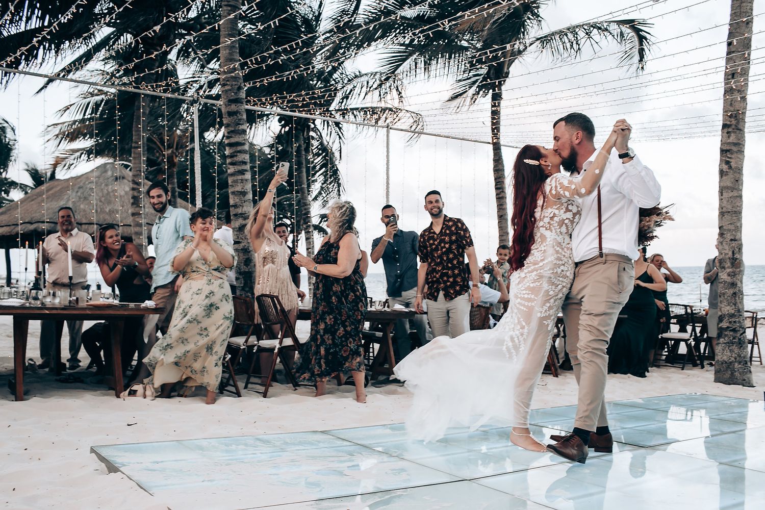 Wedding guests dance and celebrate on an outdoor patio with palm trees and ocean views during a tropical reception.