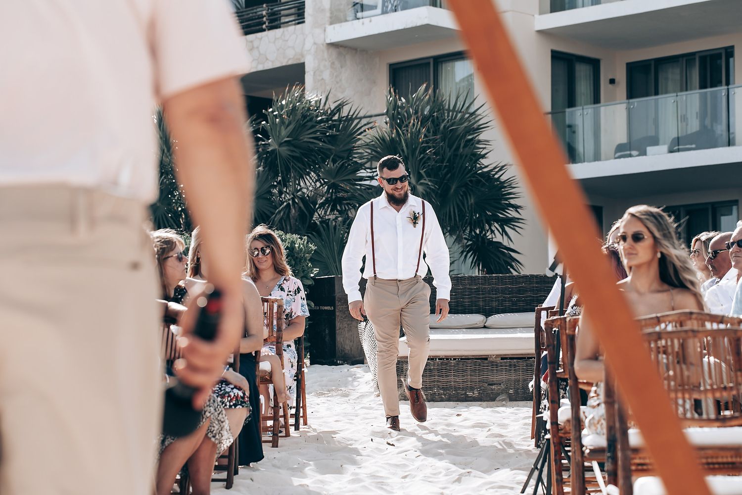 Wedding guests seated in chairs along a sandy beach path.