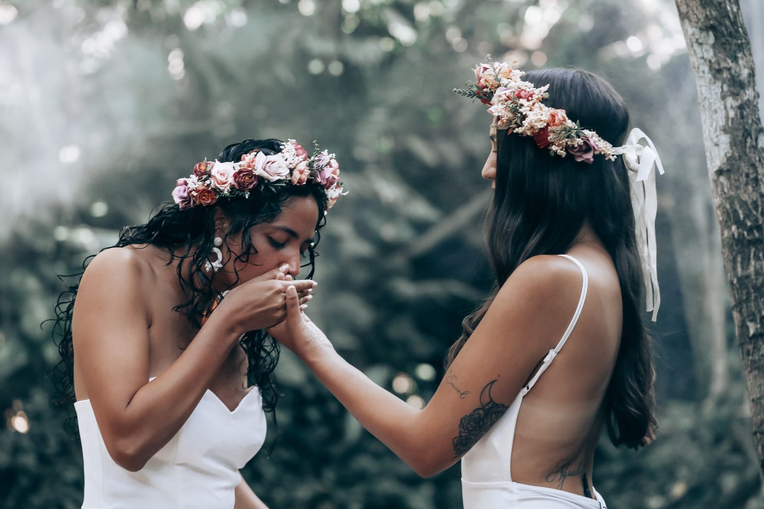 Two people in white dresses with floral crowns in a romantic forest photoshoot.