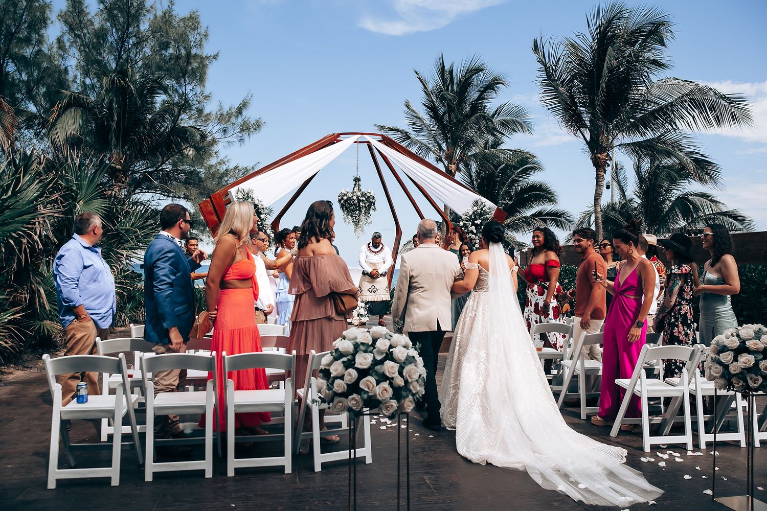 Wedding ceremony setup on a tropical beach with white chairs and palm trees swaying in the breeze.