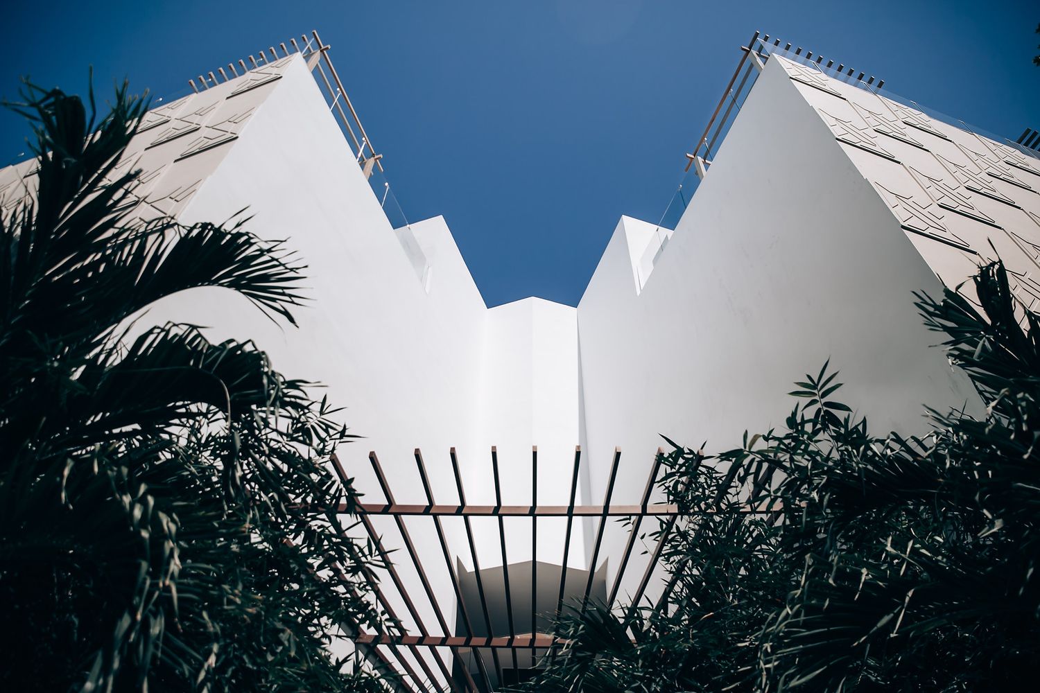 Looking up at white modern architectural building with symmetrical towers framed by palm trees against blue sky.
